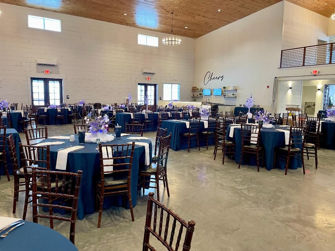 Large banquet hall with round tables set for an event and blue chairs arranged throughout