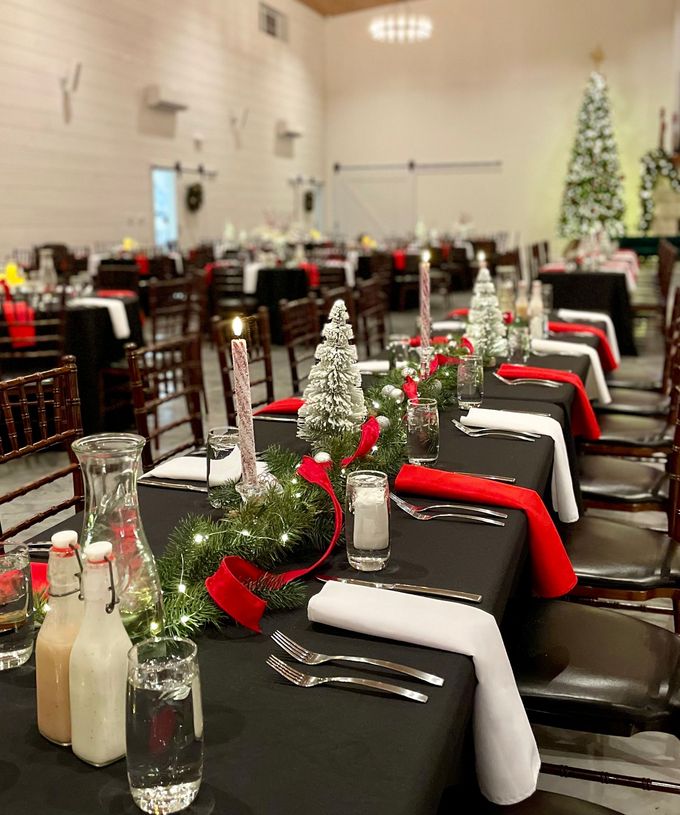 Festively decorated banquet hall with black chairs, red bows, white napkins, and lit holiday centerpieces