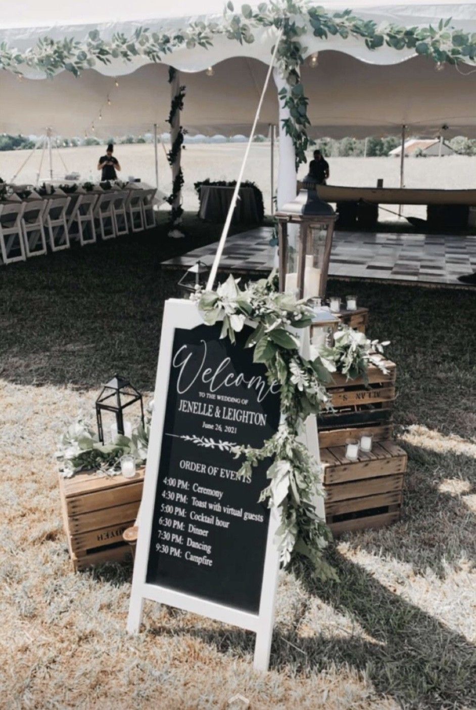 Wedding welcome sign on easel beside floral-decorated tent and tables at an outdoor reception