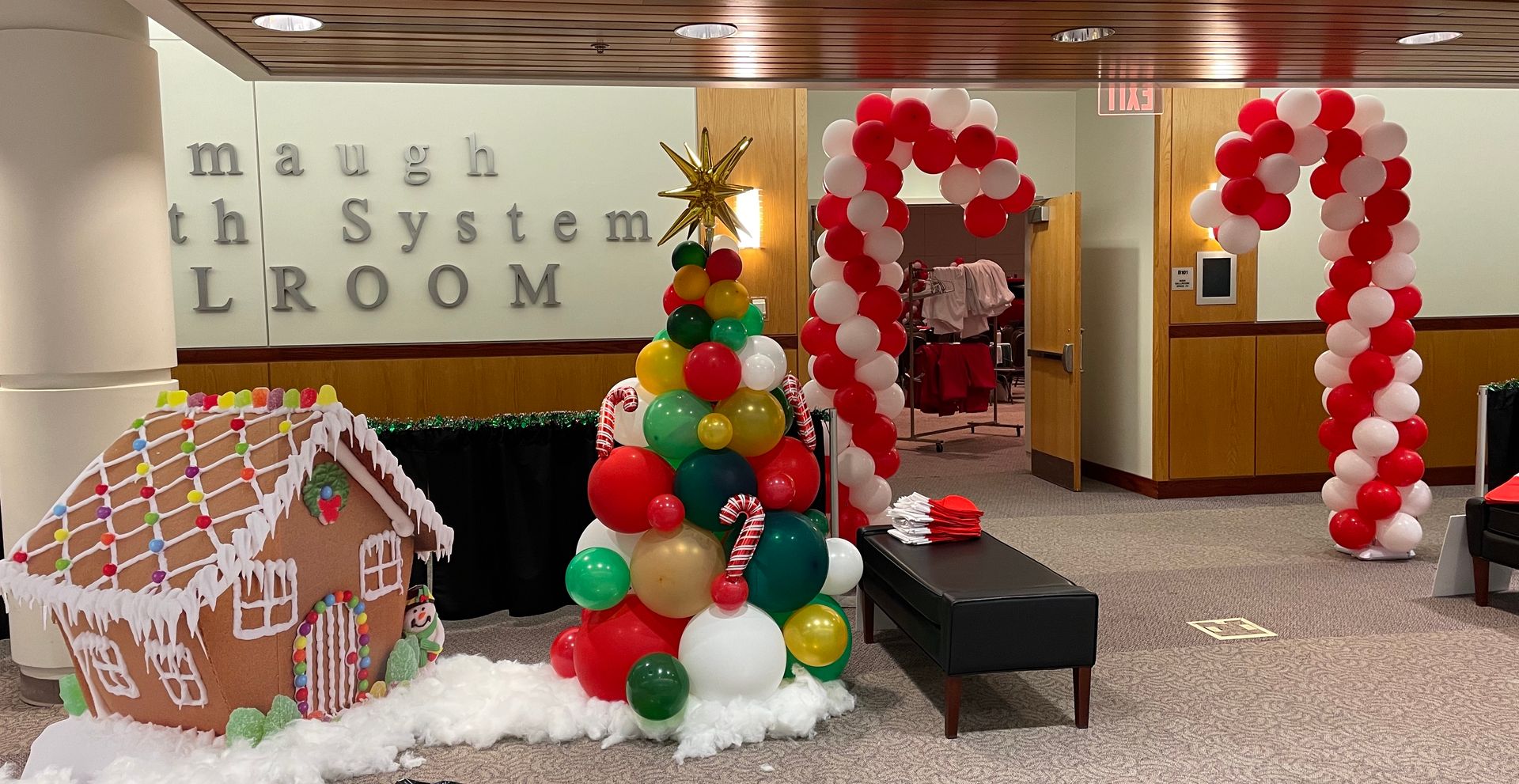 Holiday display in a lobby with a gingerbread house, Christmas tree, and red-and-white balloon arches