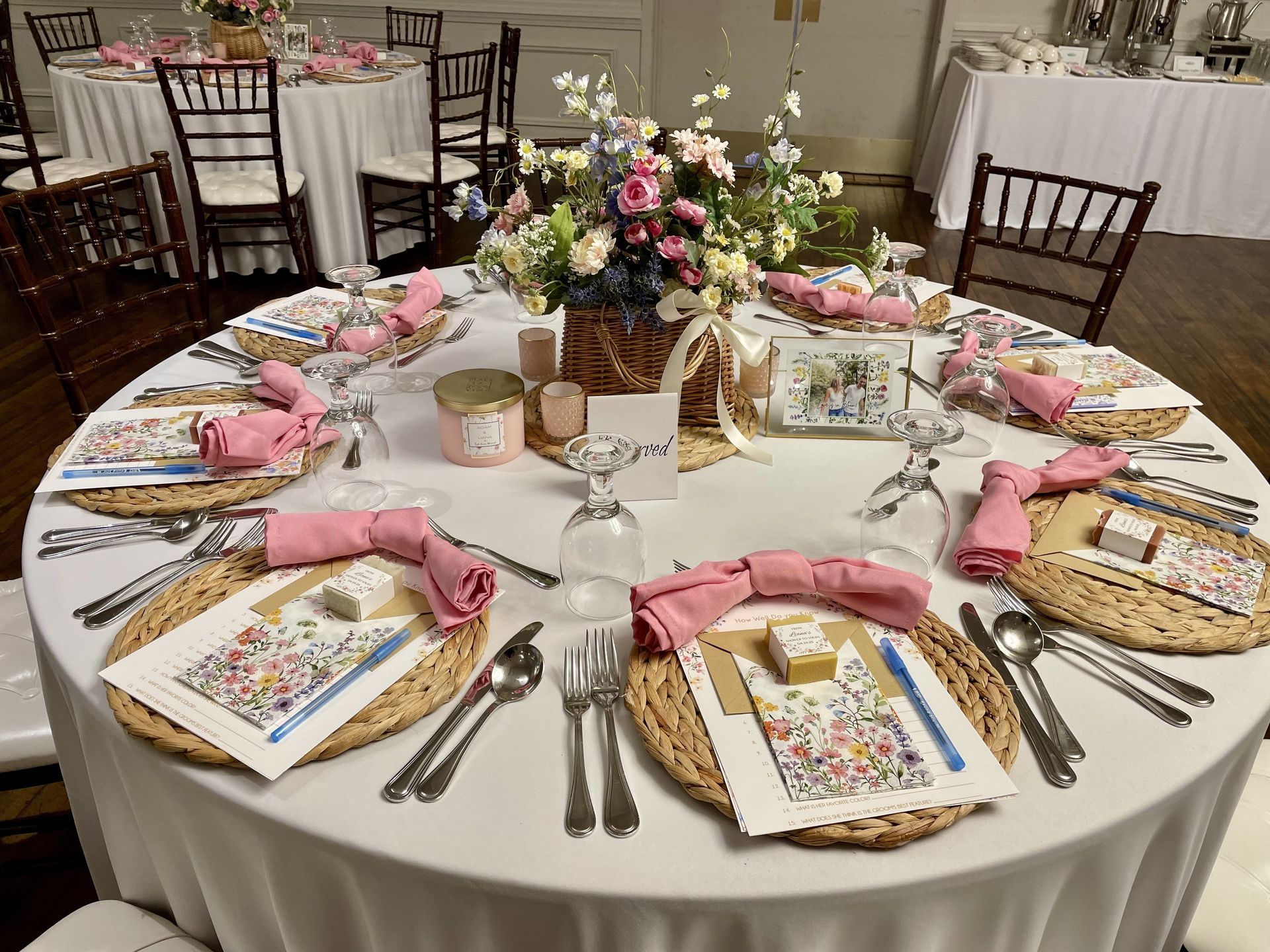 Round banquet table set with pink napkins, gold utensils, floral centerpieces, and decorated place cards