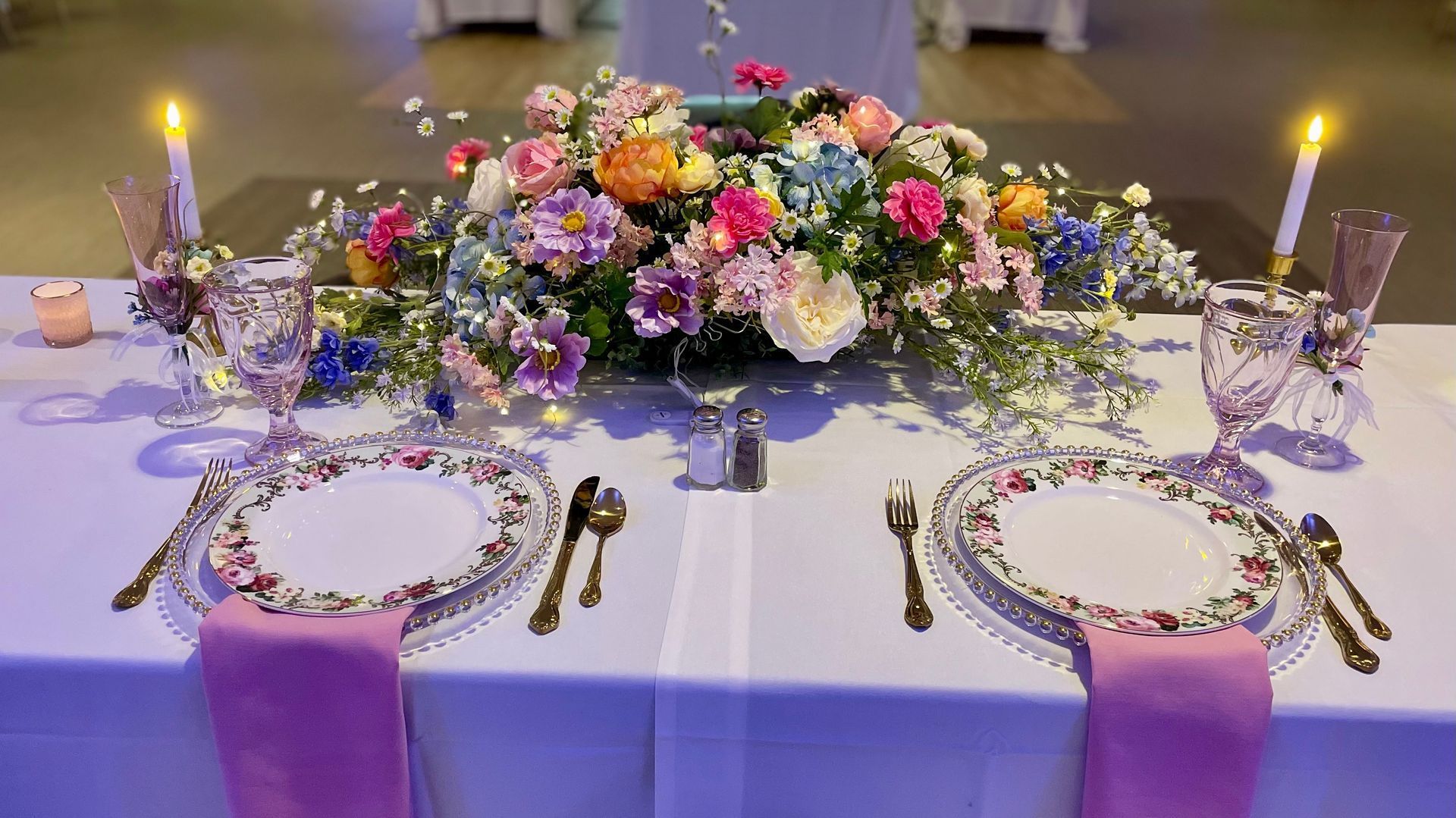 Elegant wedding reception table with white linens, floral centerpiece, candles, and pink napkins set for two