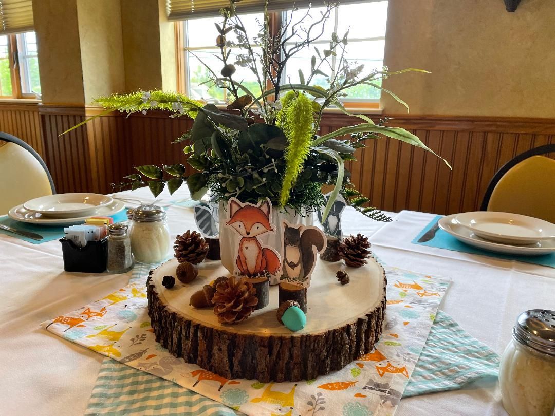 Decorated cake centerpiece with forest-themed figurines and flowers on a dining table in a restaurant