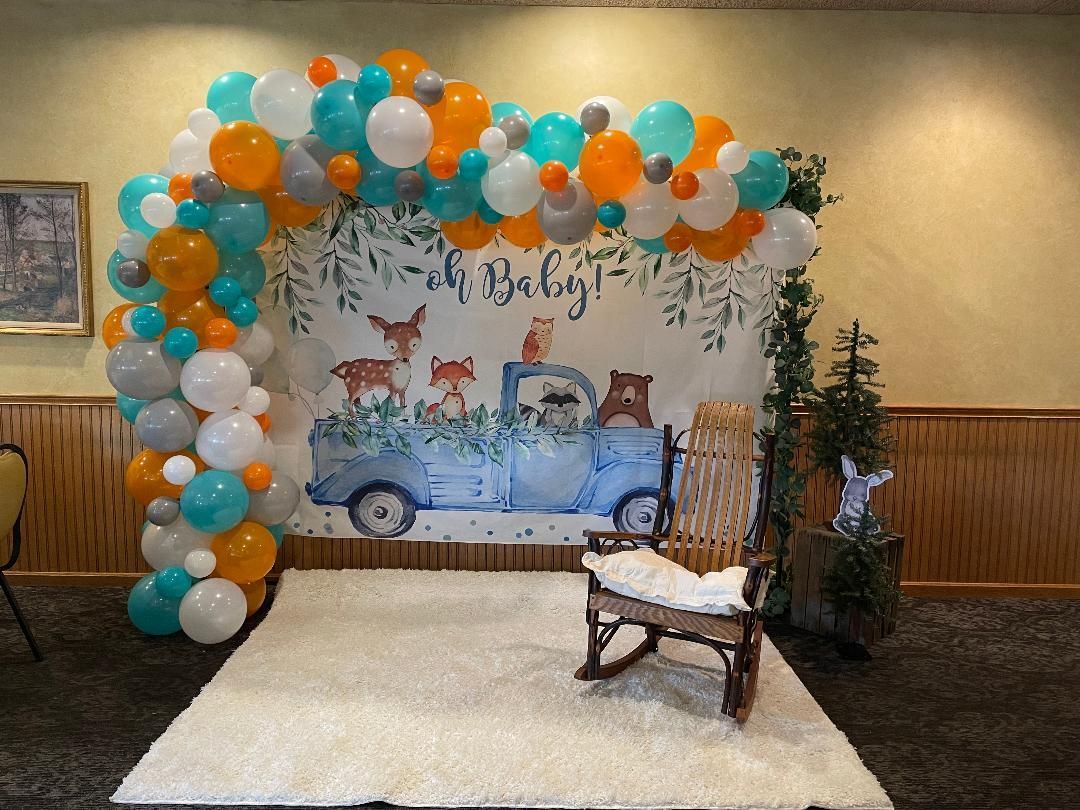 Blue truck birthday backdrop with teal, orange, and white balloons, a rug, and a chair display