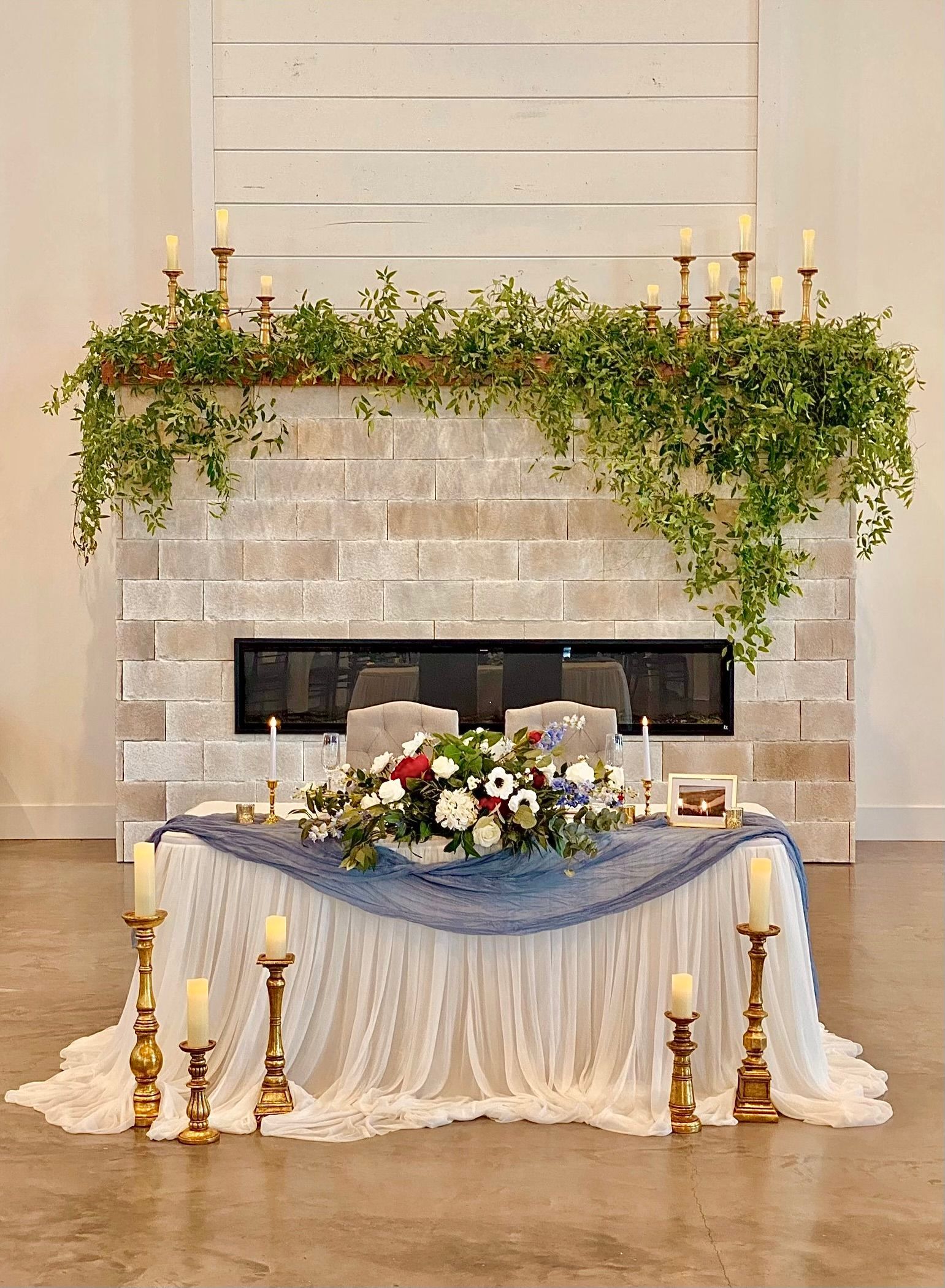 Decorated fireplace with greenery, candles, and a white draped table topped with flowers in a formal room