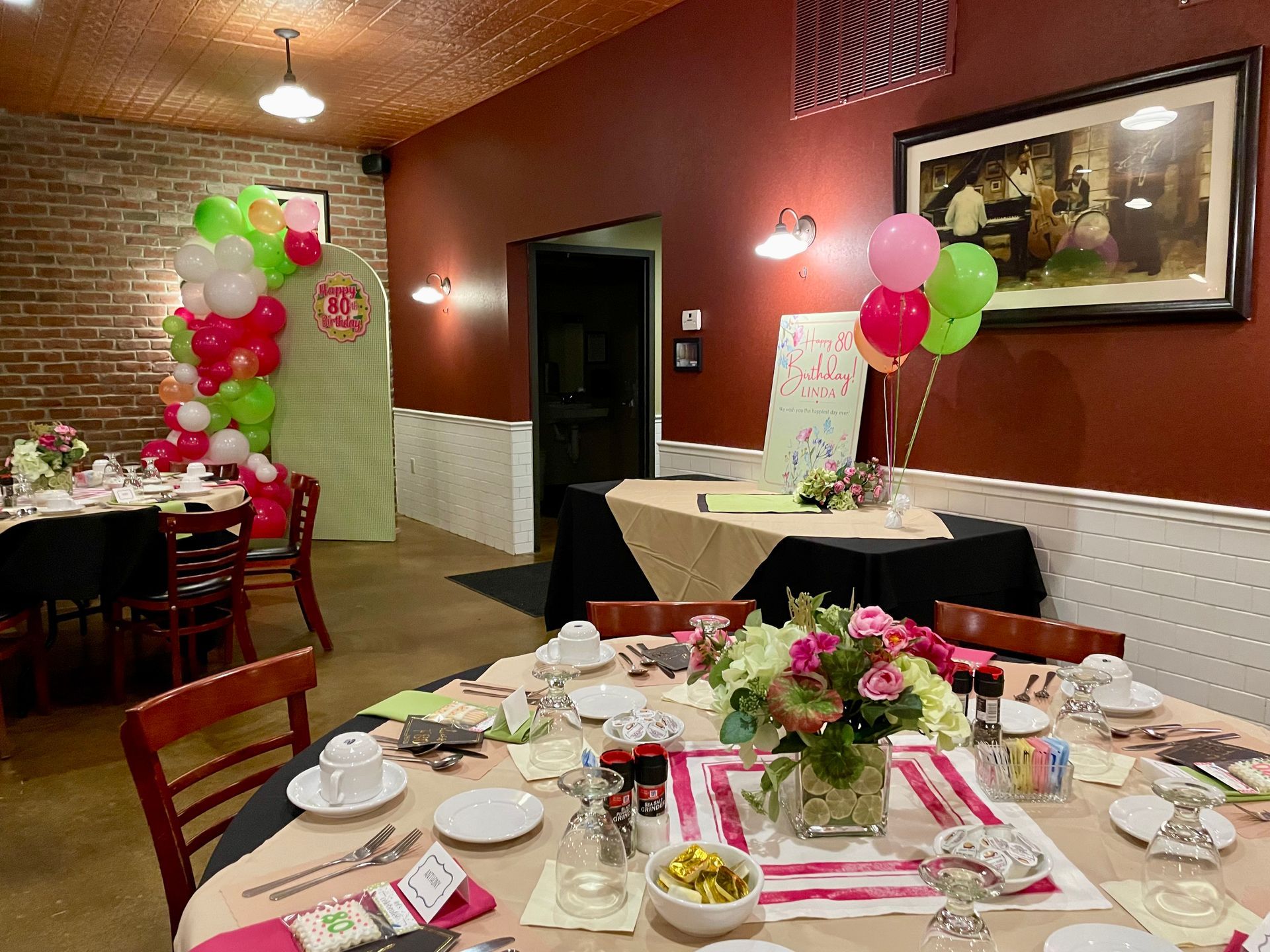 Decorated banquet room with set tables, red and green balloons, and pink floral centerpieces