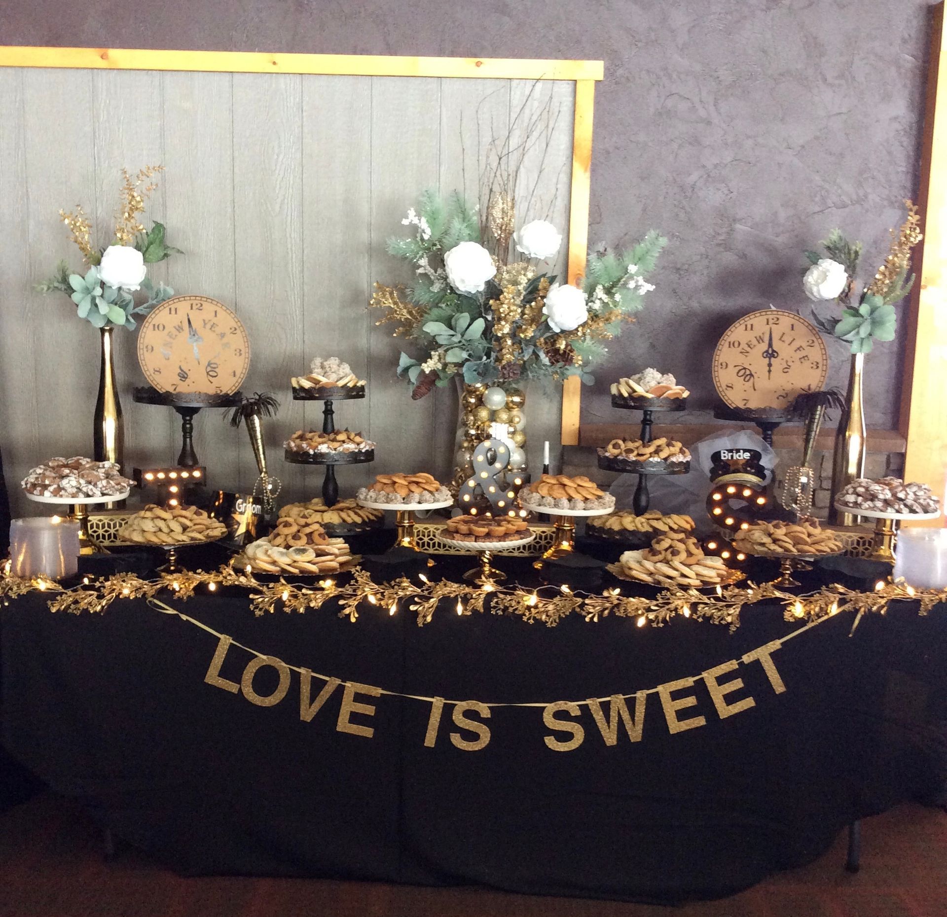 Elegant dessert buffet with gold accents, floral decor, and a black tablecloth reading “LOVE IS SWEET”