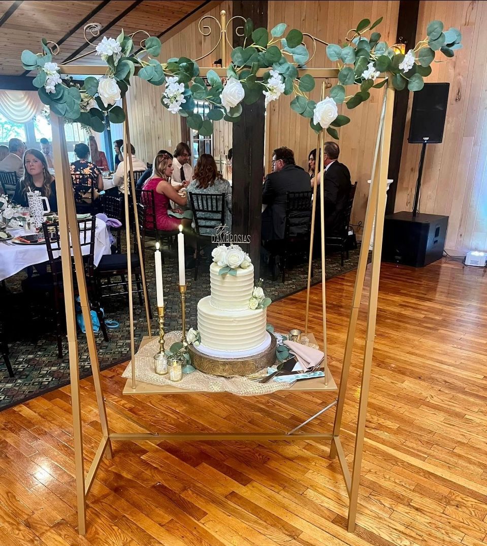 Decorated wedding cake on a gold stand under a floral arch in a banquet hall