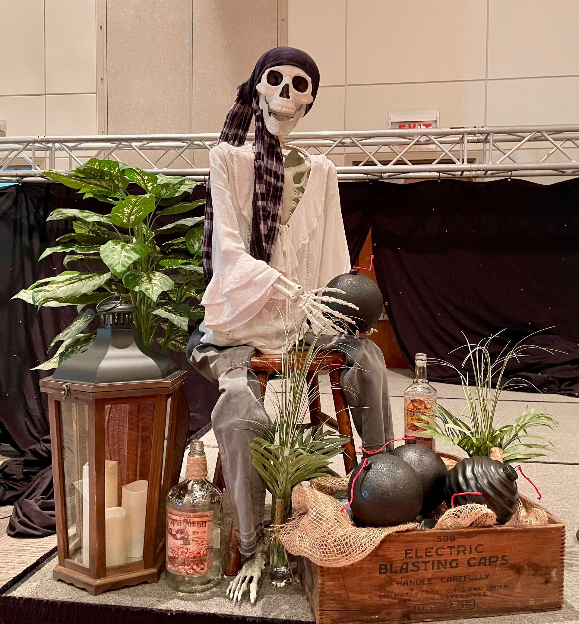 Skeleton figure sitting among Halloween decorations and plants on a table indoors