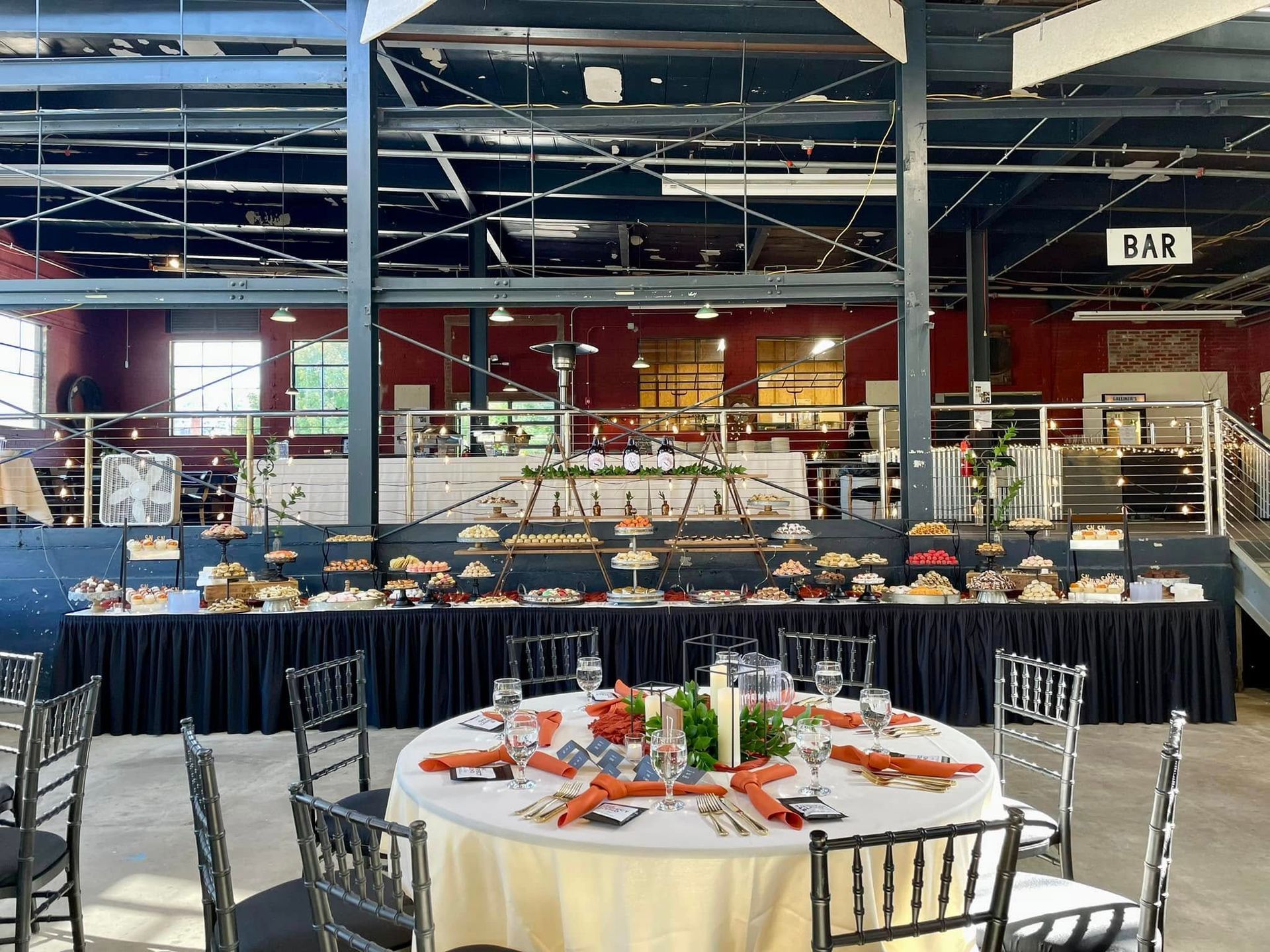 Banquet tables set with flowers in a large indoor event hall, with a bar in the background