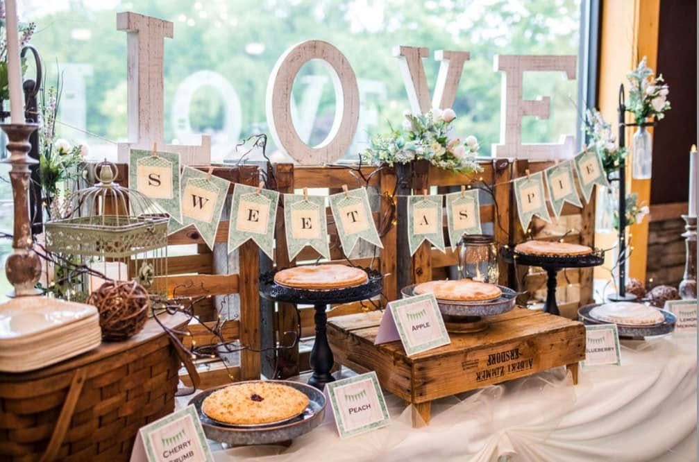 Rustic dessert table with LOVE letters, banner, candles, cakes, and decor by a bright window
