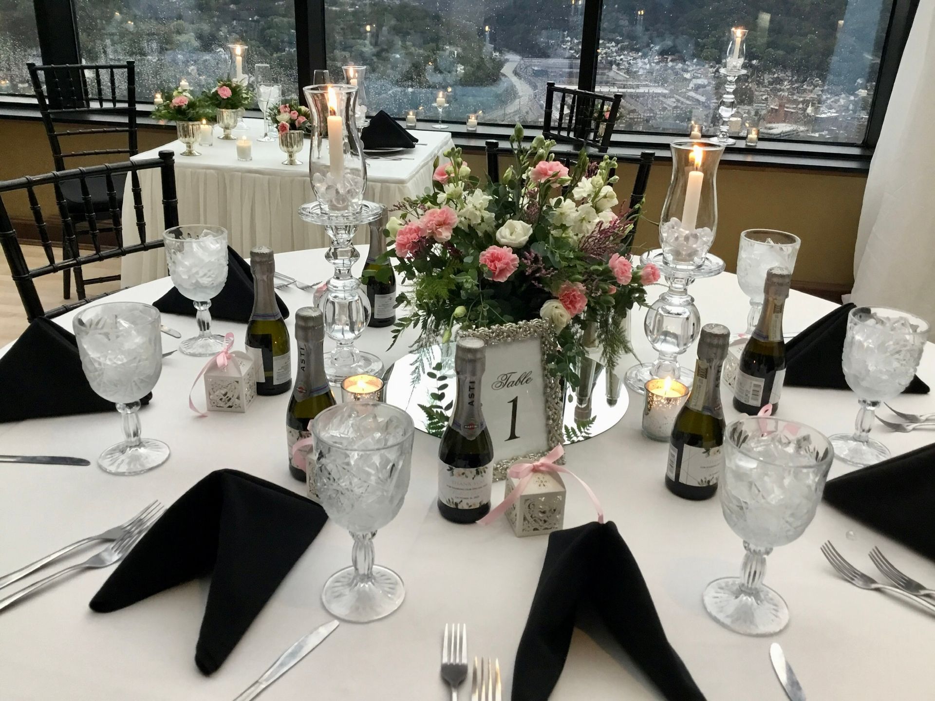 Elegant banquet table with floral centerpiece, candles, wine bottles, and black napkins by a window