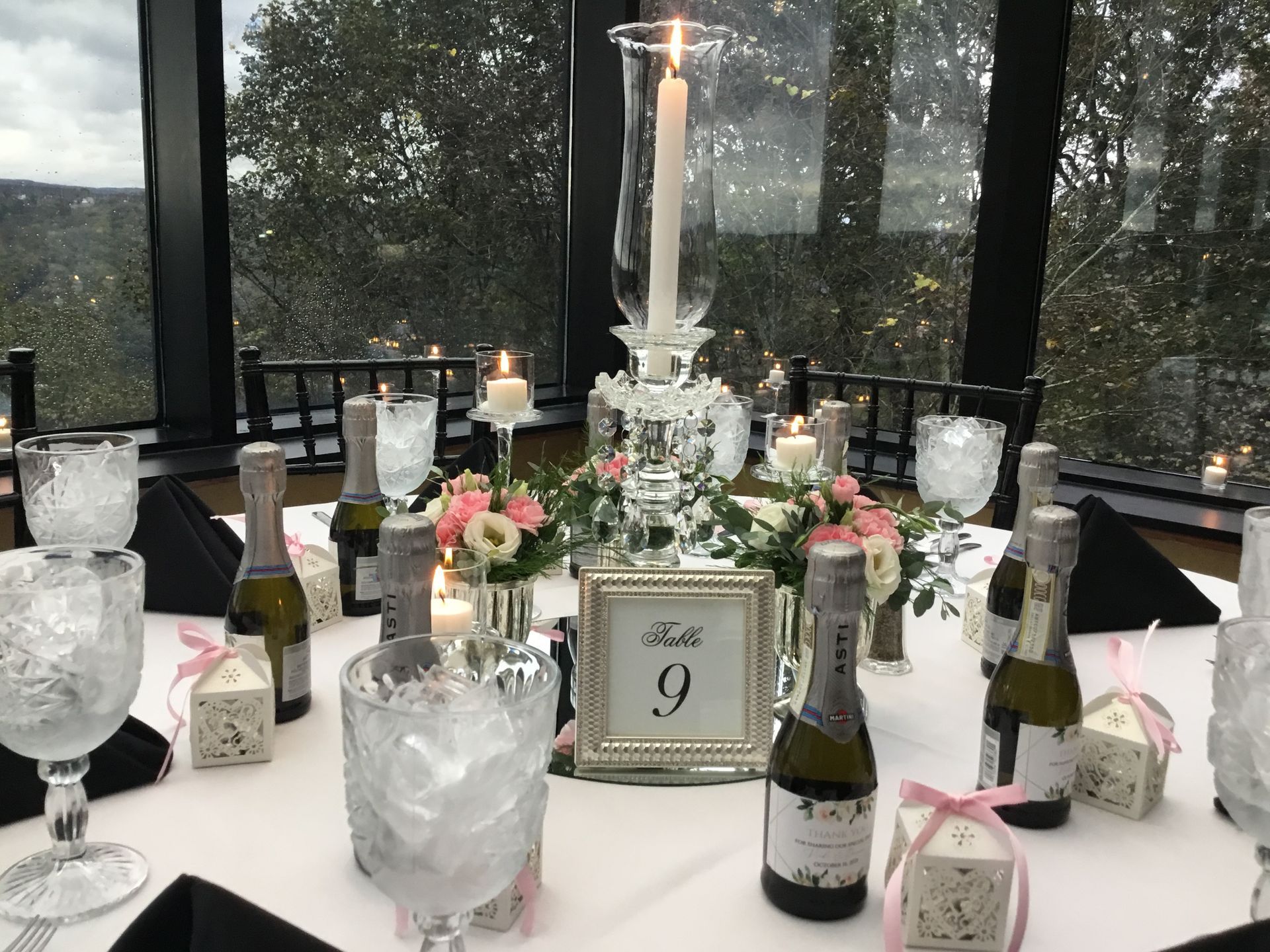 Elegant table centerpiece with candles, flowers, wine bottles, and a table card numbered 9 in a glass room