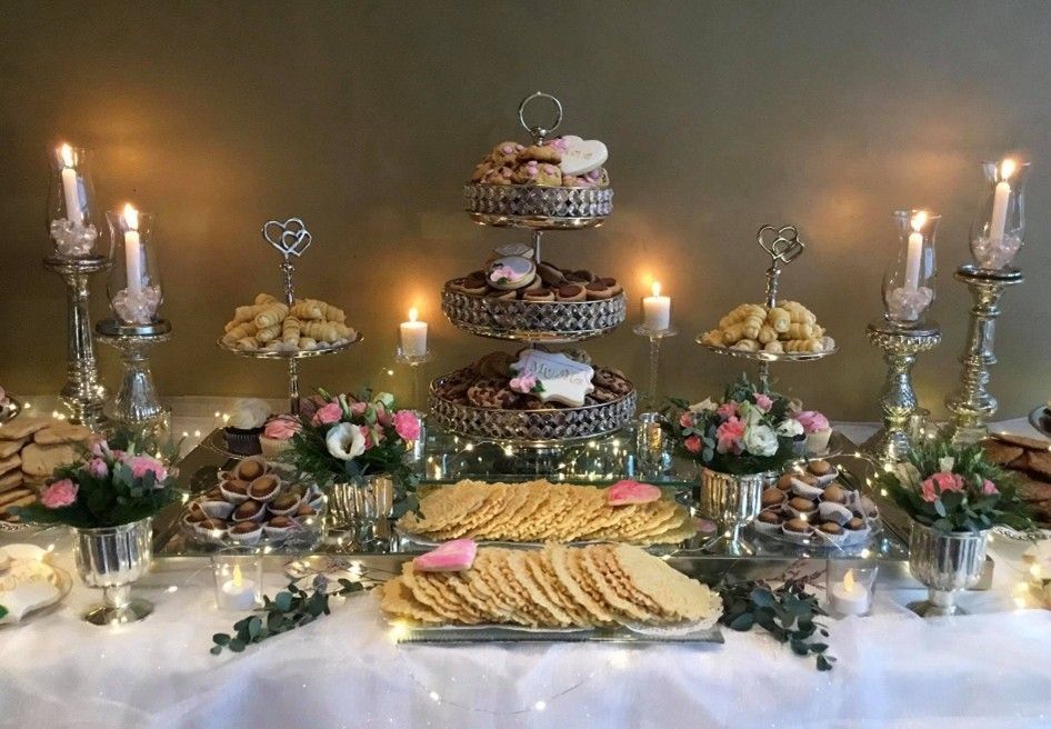 Elegant dessert table with tiered treats, candles, floral arrangements, and platters of cookies and pastries
