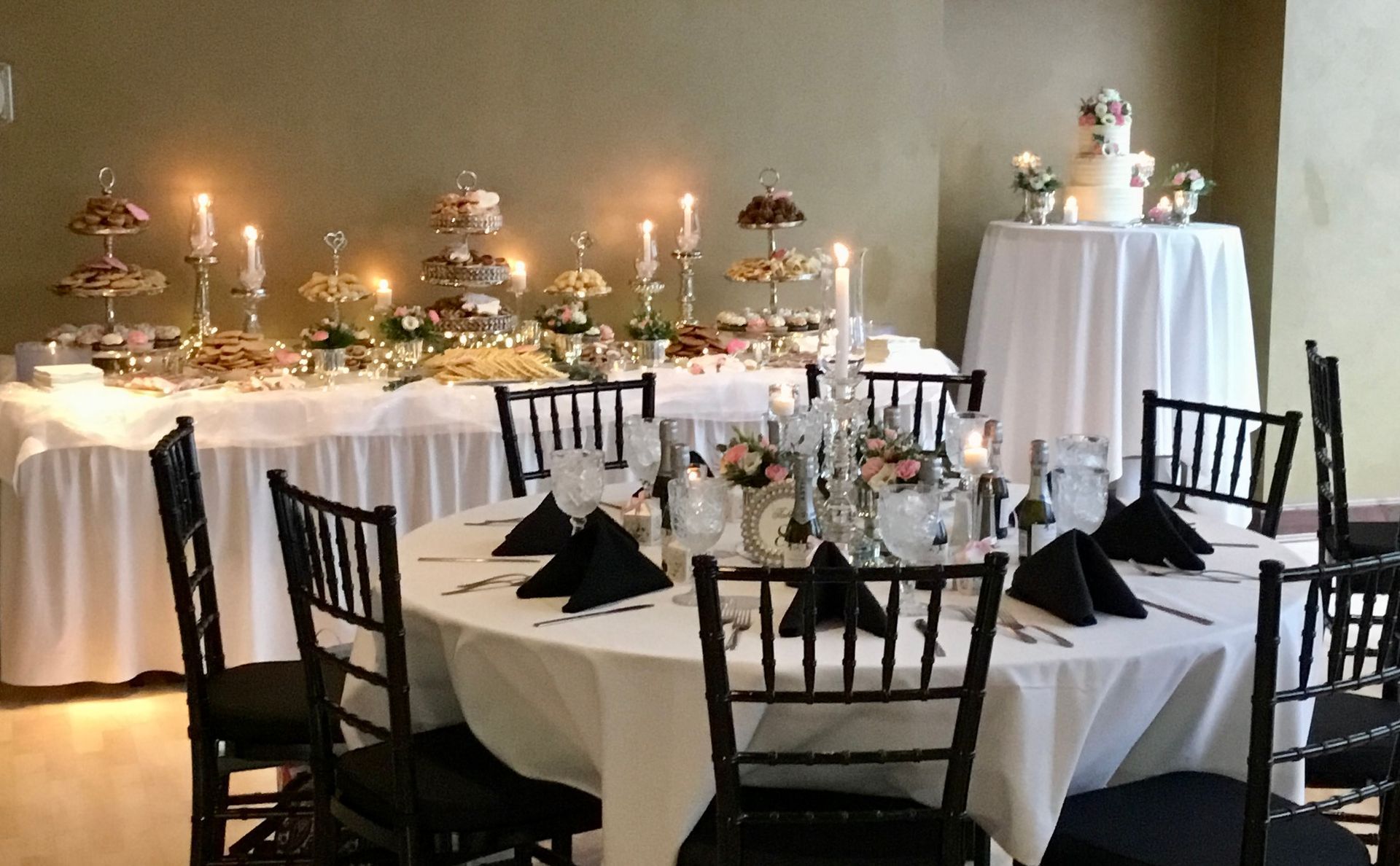 Elegant banquet hall with round tables, black chairs, white tablecloths, candles, and floral centerpieces.