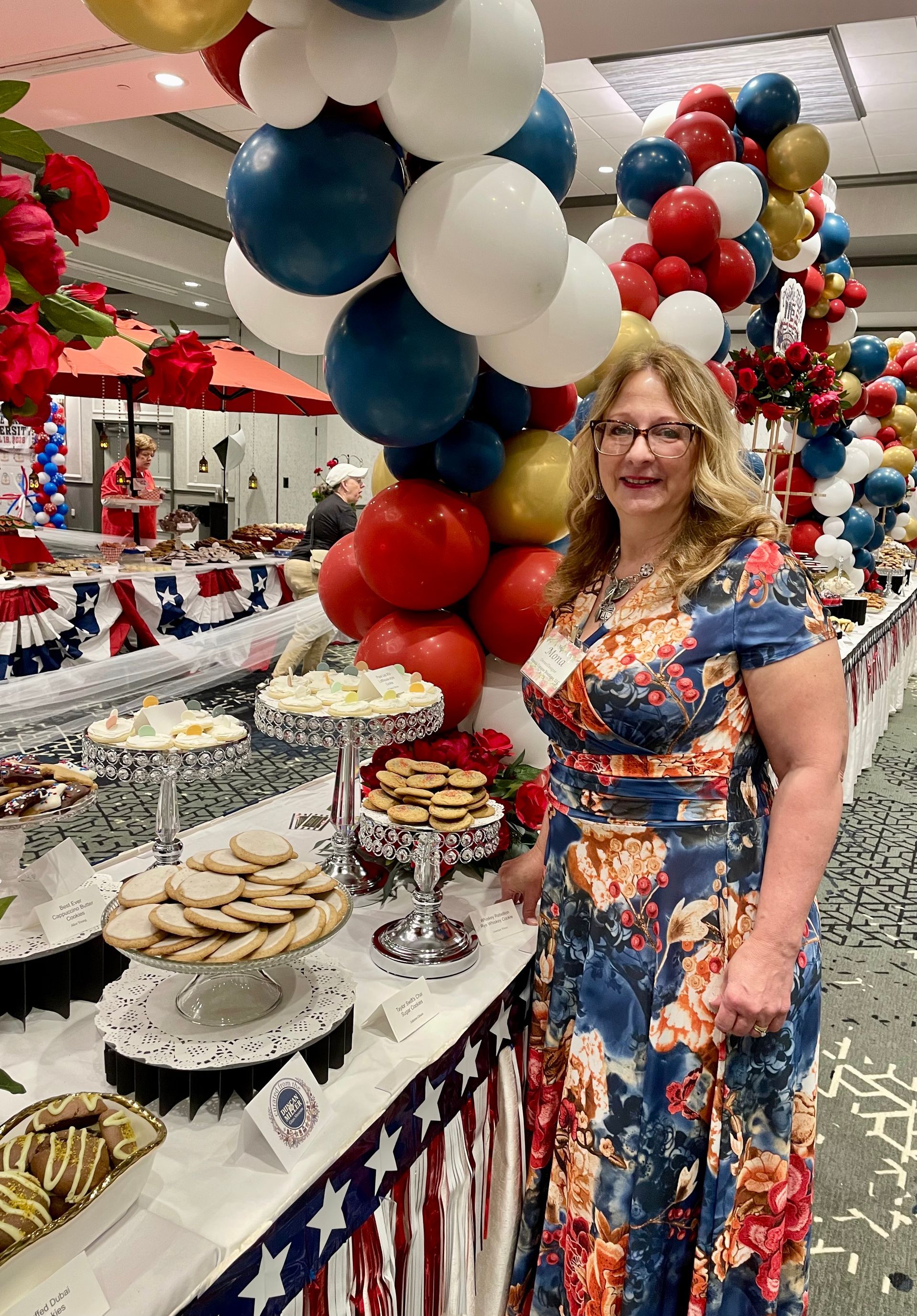 Woman standing by a patriotic dessert table with red, white, and blue decorations and balloon arch