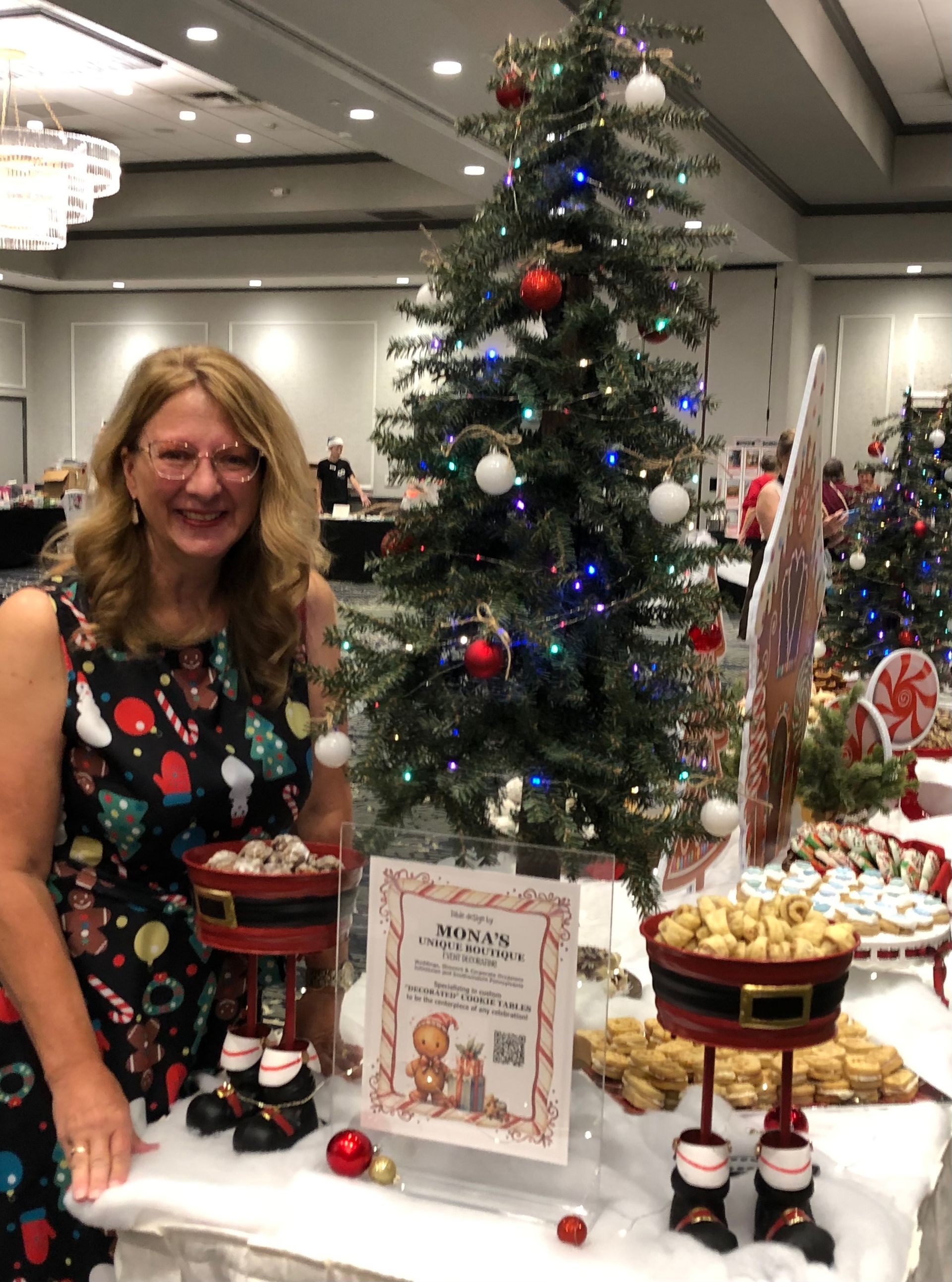Woman standing beside a decorated Christmas display at an indoor holiday event