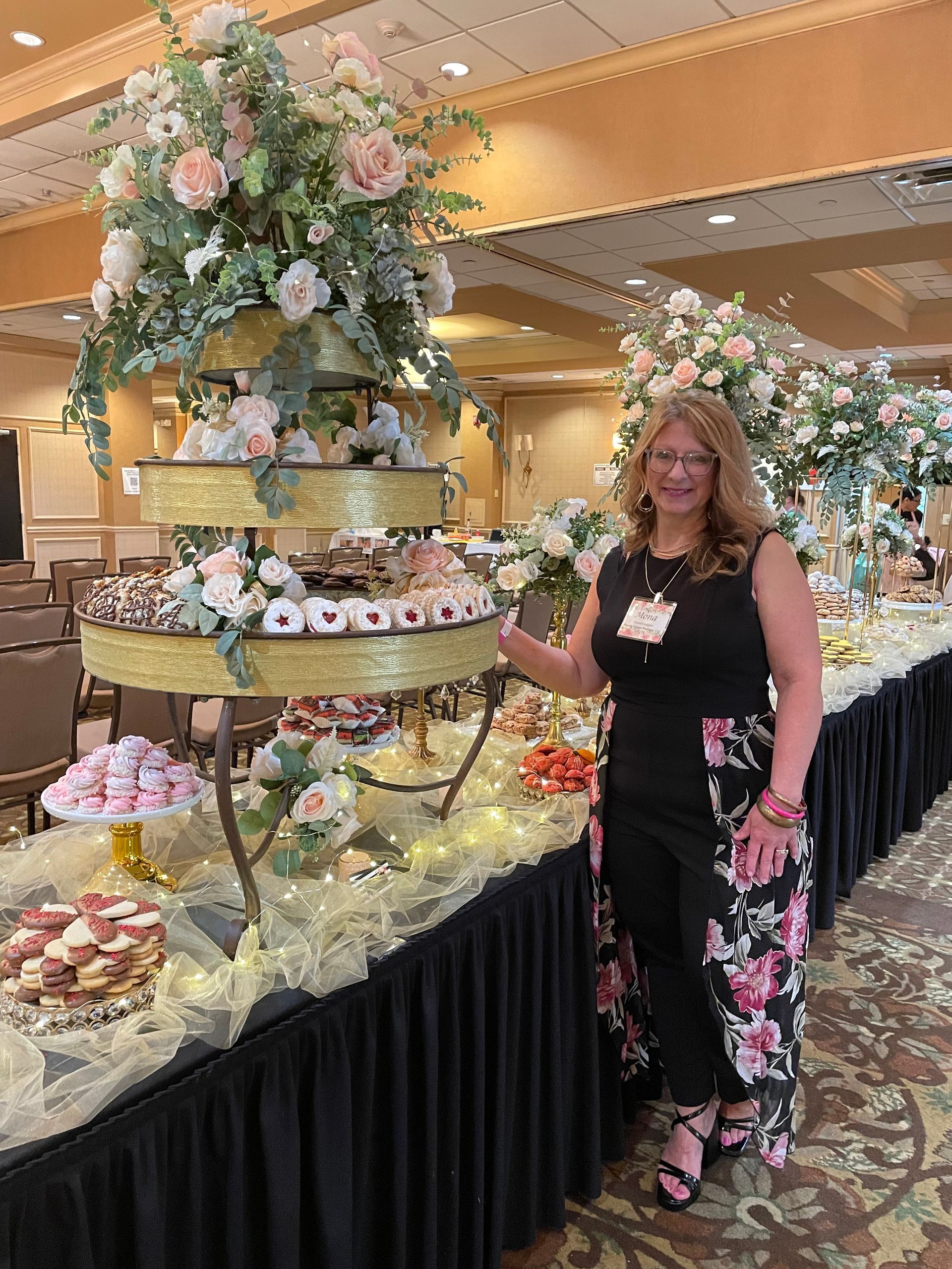 Woman standing beside a tiered dessert display at a buffet table in a banquet hall