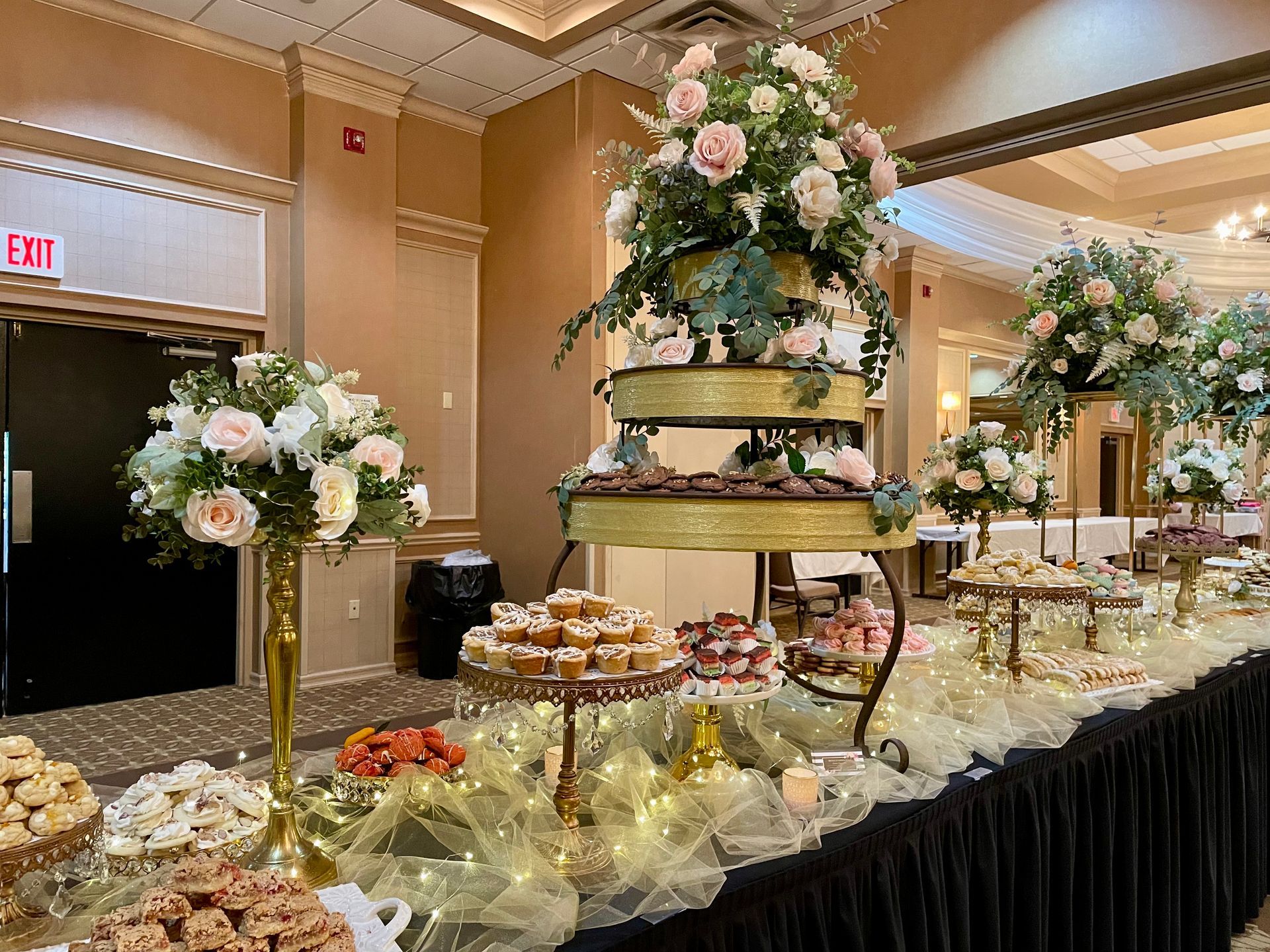 Elegant banquet dessert table with tiered floral centerpieces and assorted pastries in a ballroom