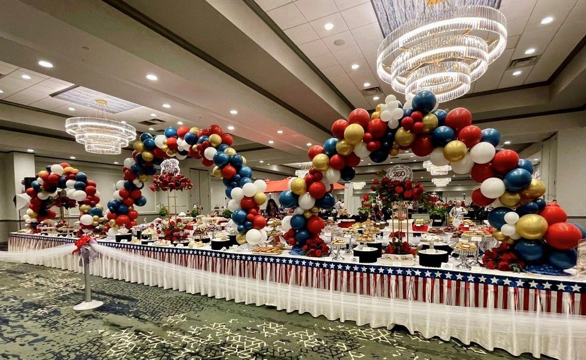 Balloon arches and colorful table decor in a large banquet hall with chandeliers