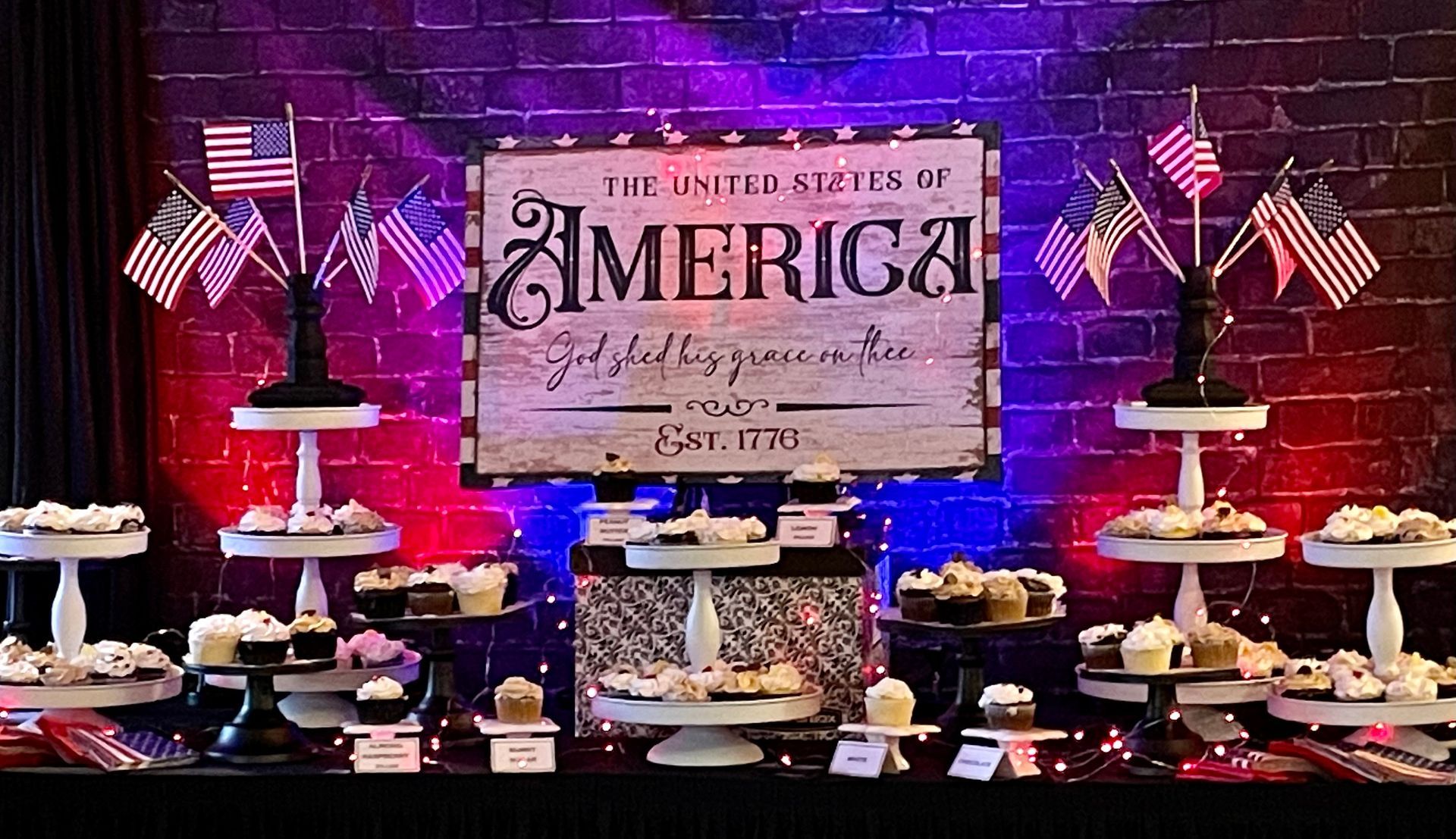Patriotic dessert table with red, white, and blue treats, American flags, and a “The Best in America” sign