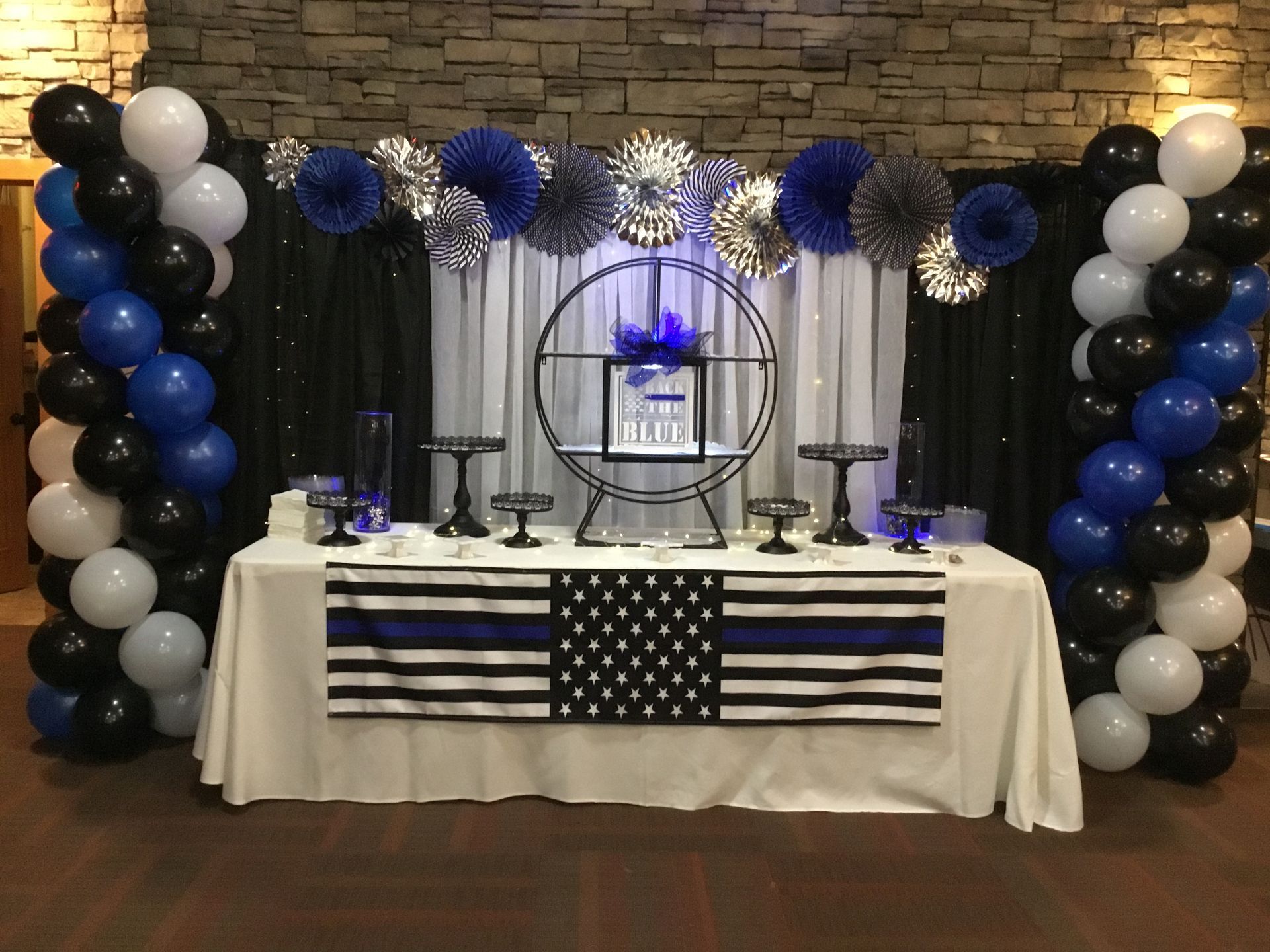 Black, white, and blue balloon-decorated memorial table with candles and flag backdrop