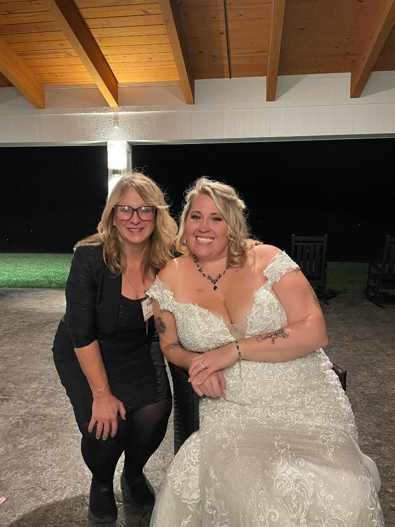 Two women posing together under a wooden pavilion, smiling, one in a white dress and one in black.
