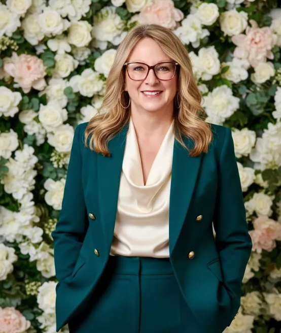 Woman in a teal suit smiling before a white flower wall