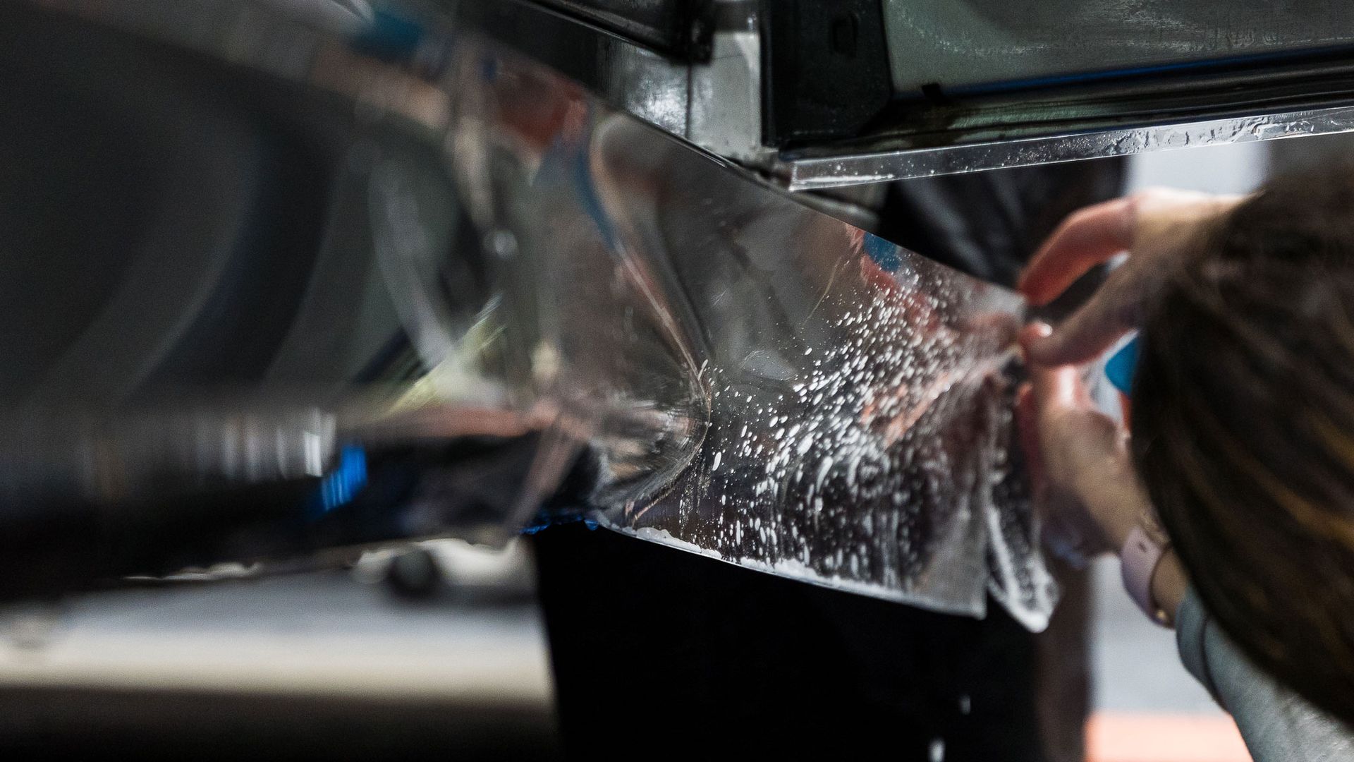 A person is wrapping a piece of plastic on a car.
