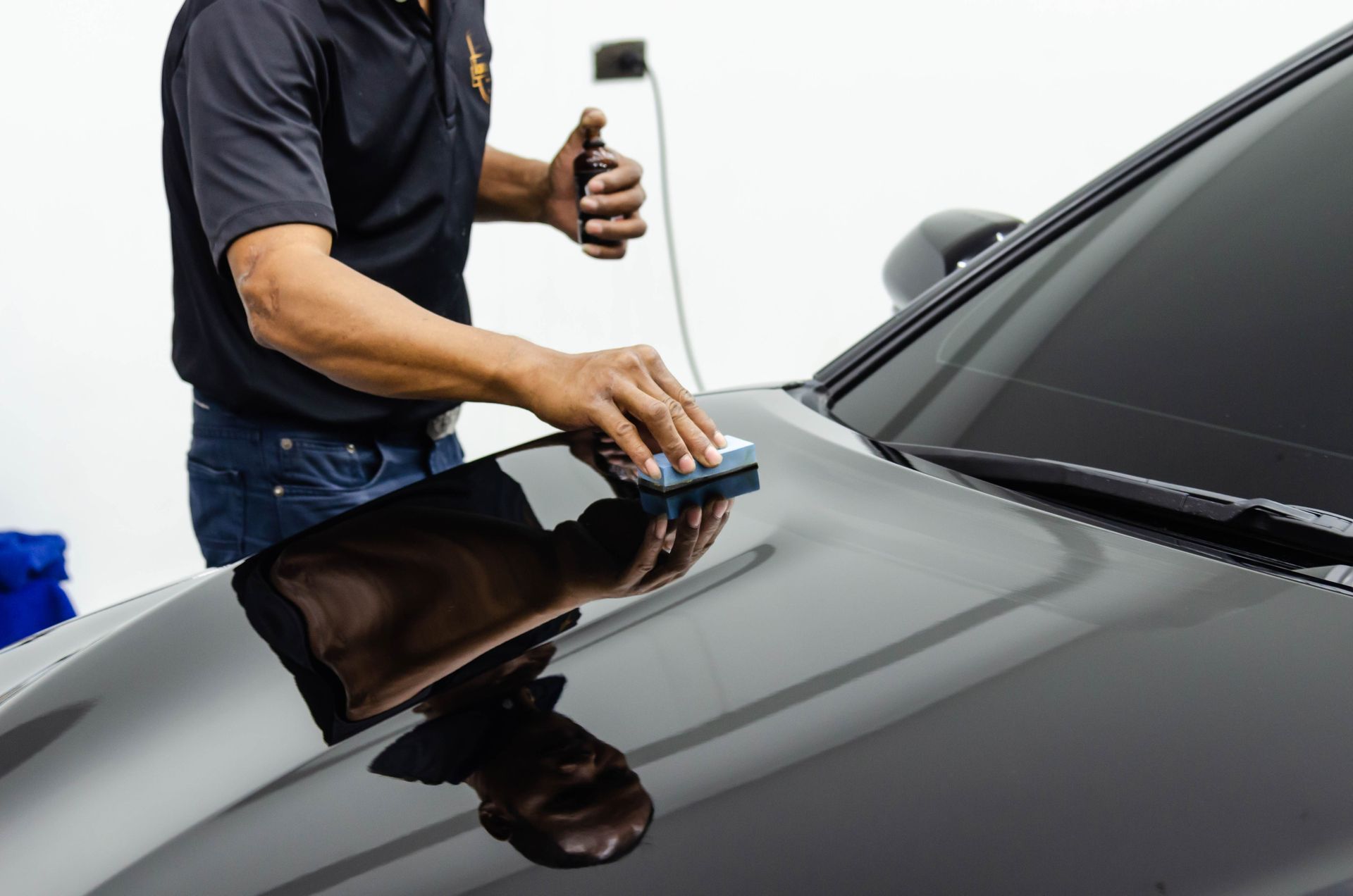 A man is polishing the hood of a black car.