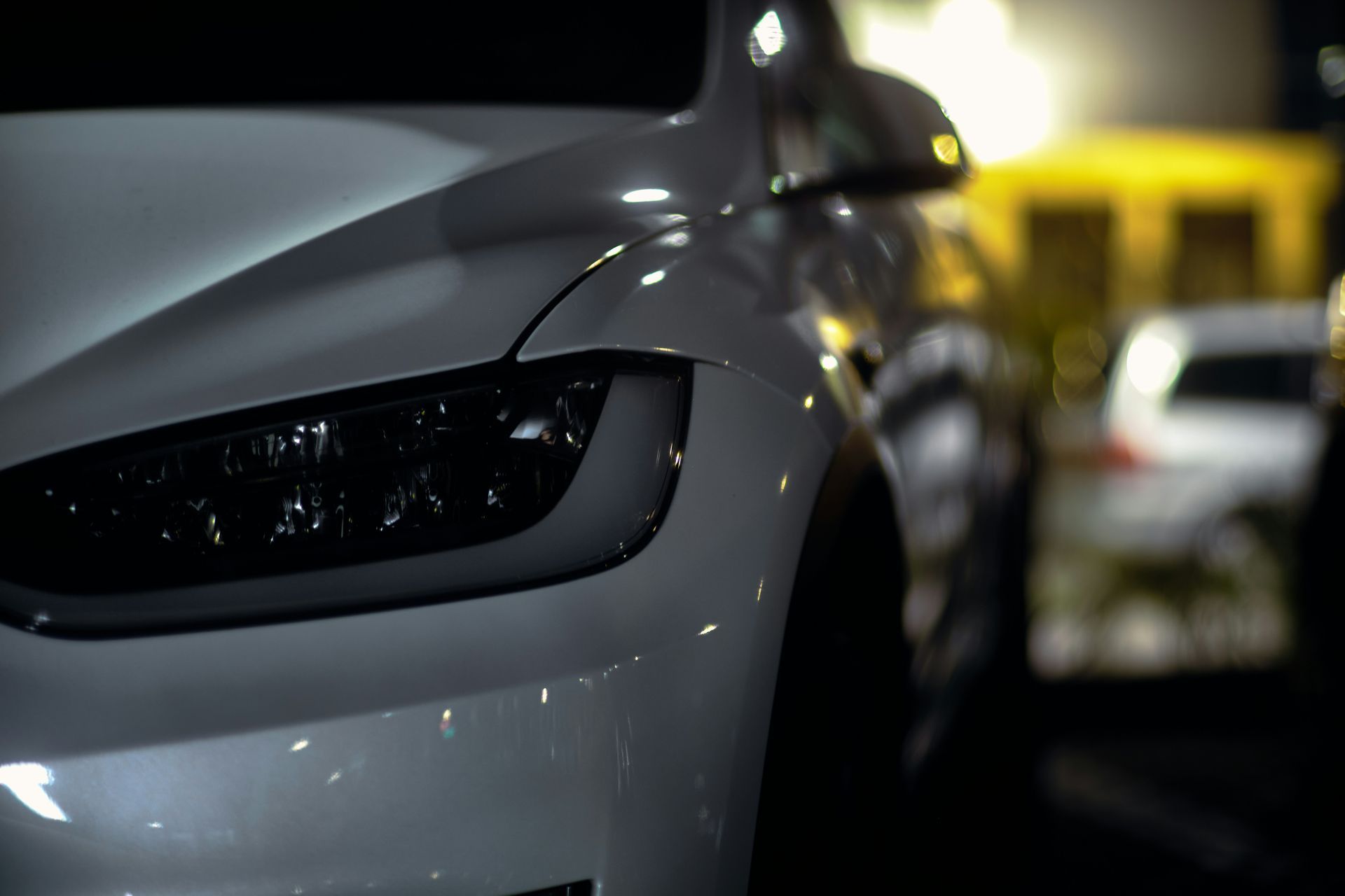 A close up of a white car parked in a parking lot at night.