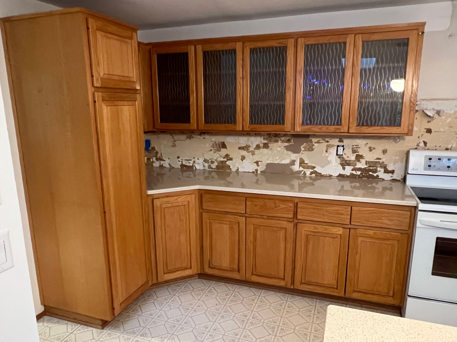 Kitchen with wooden cabinets and peeling backsplash. White countertops and stove.