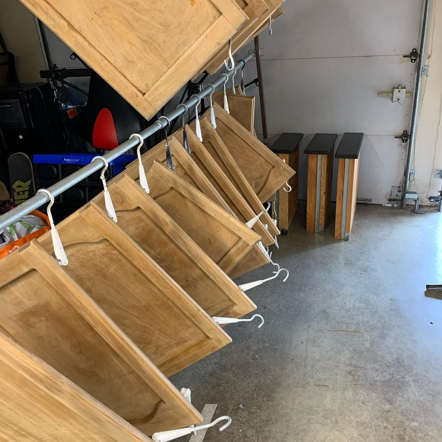 Wooden cabinet doors hanging on a metal rod with white hangers, drying in a garage.