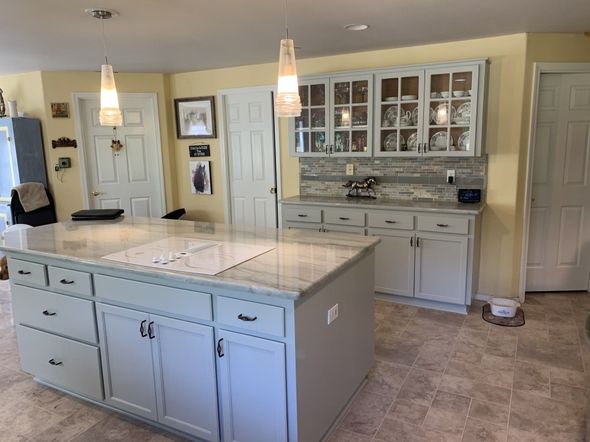 Kitchen with a large island and light blue cabinets, with pendant lights above.
