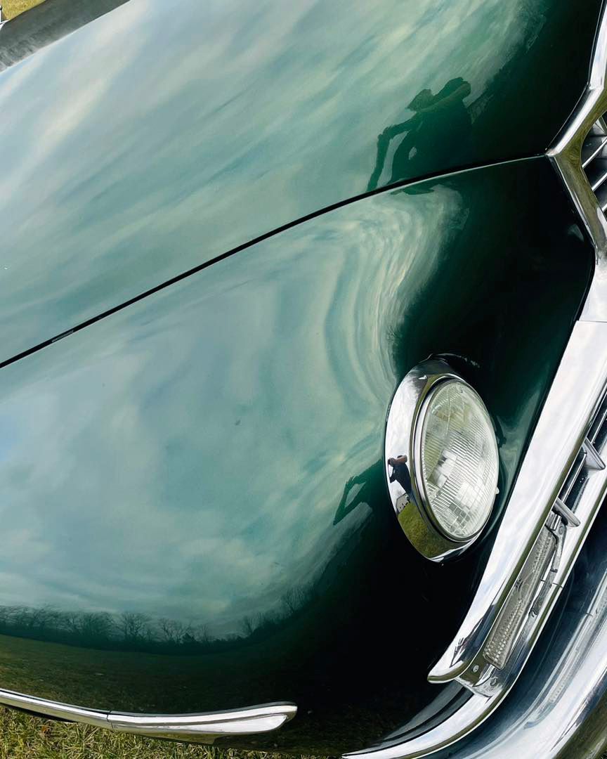 Green classic car, close-up of the hood and headlight, with a shiny, reflective surface.