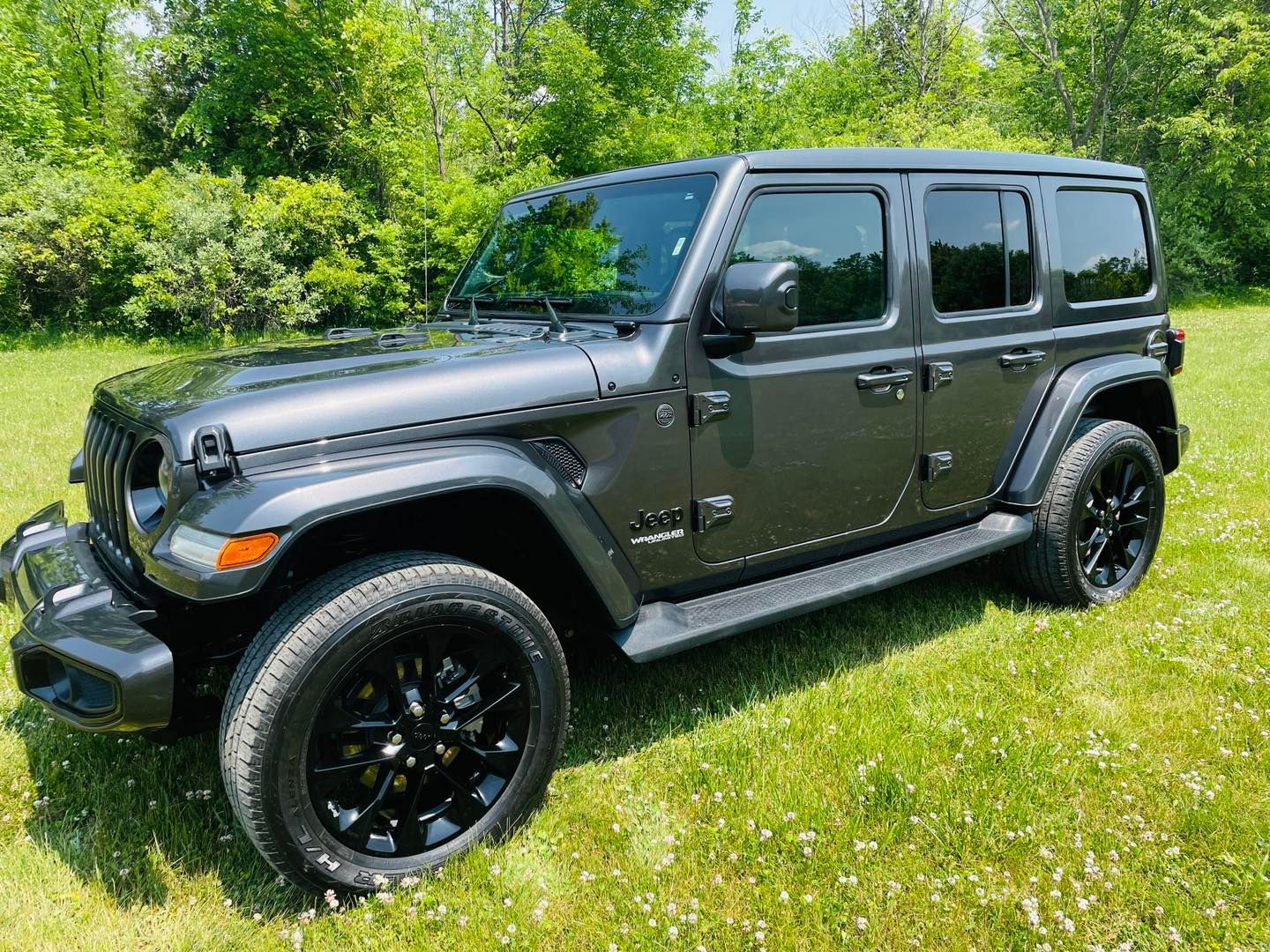 Gray Jeep Wrangler on grass with black wheels.