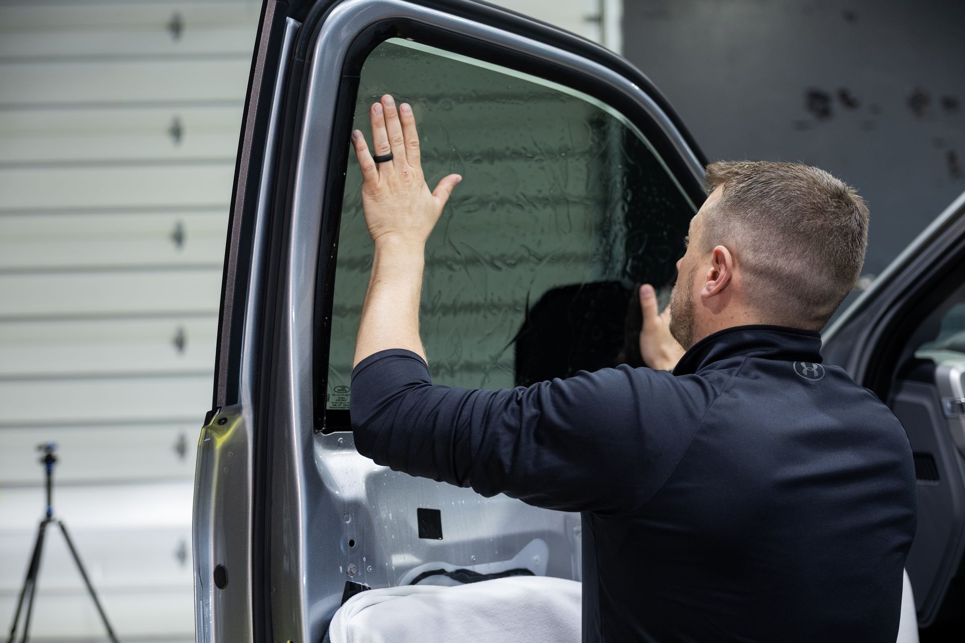 Man applying tinted film to a car window. He's inside, with the door open, using both hands.