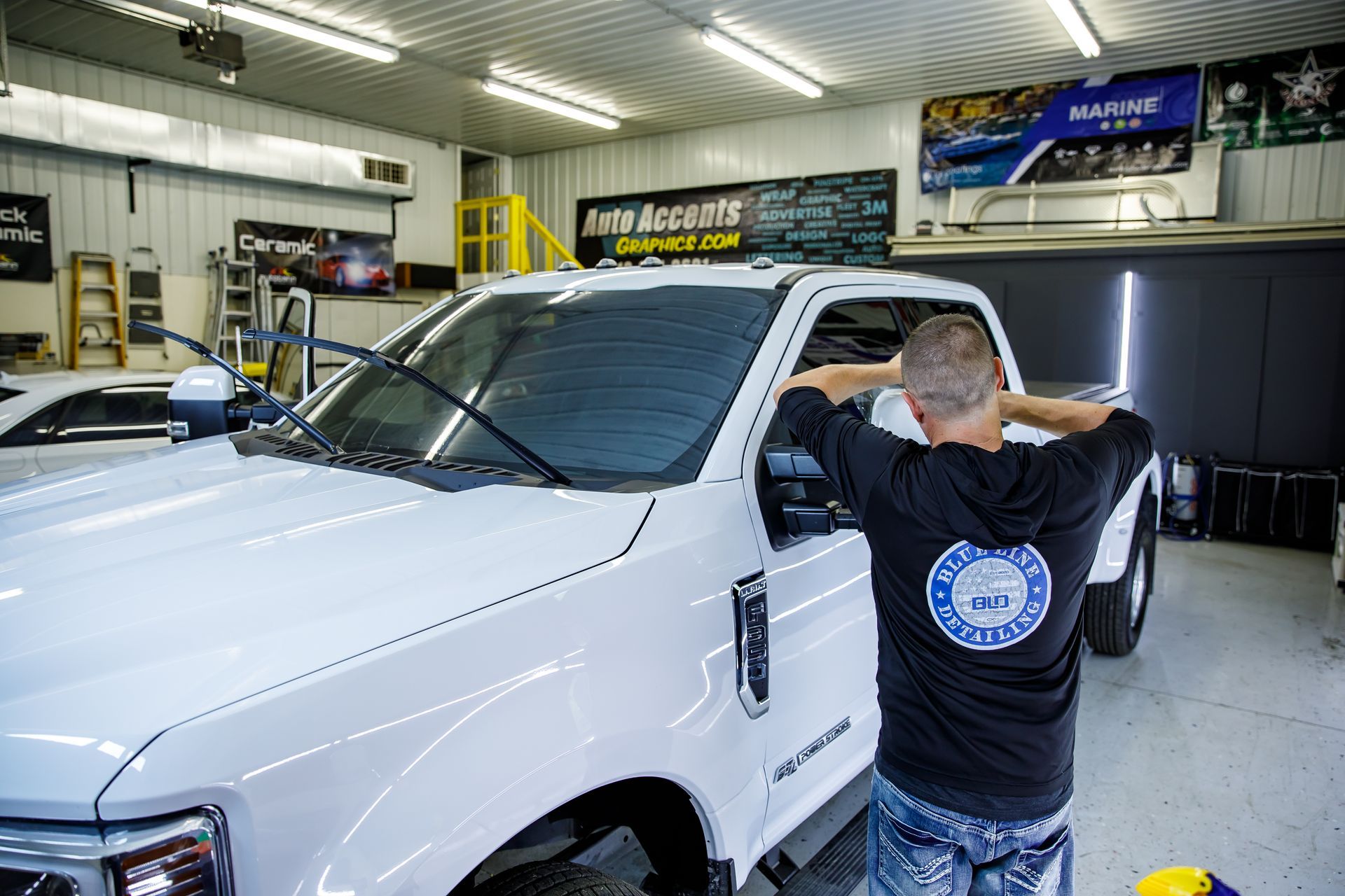 Man applying tint to a white truck windshield in a garage.