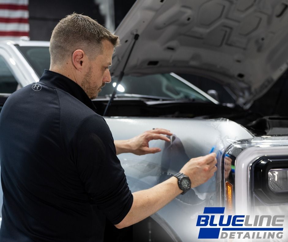 Man applying protective film to the front of a silver truck in a detail shop.