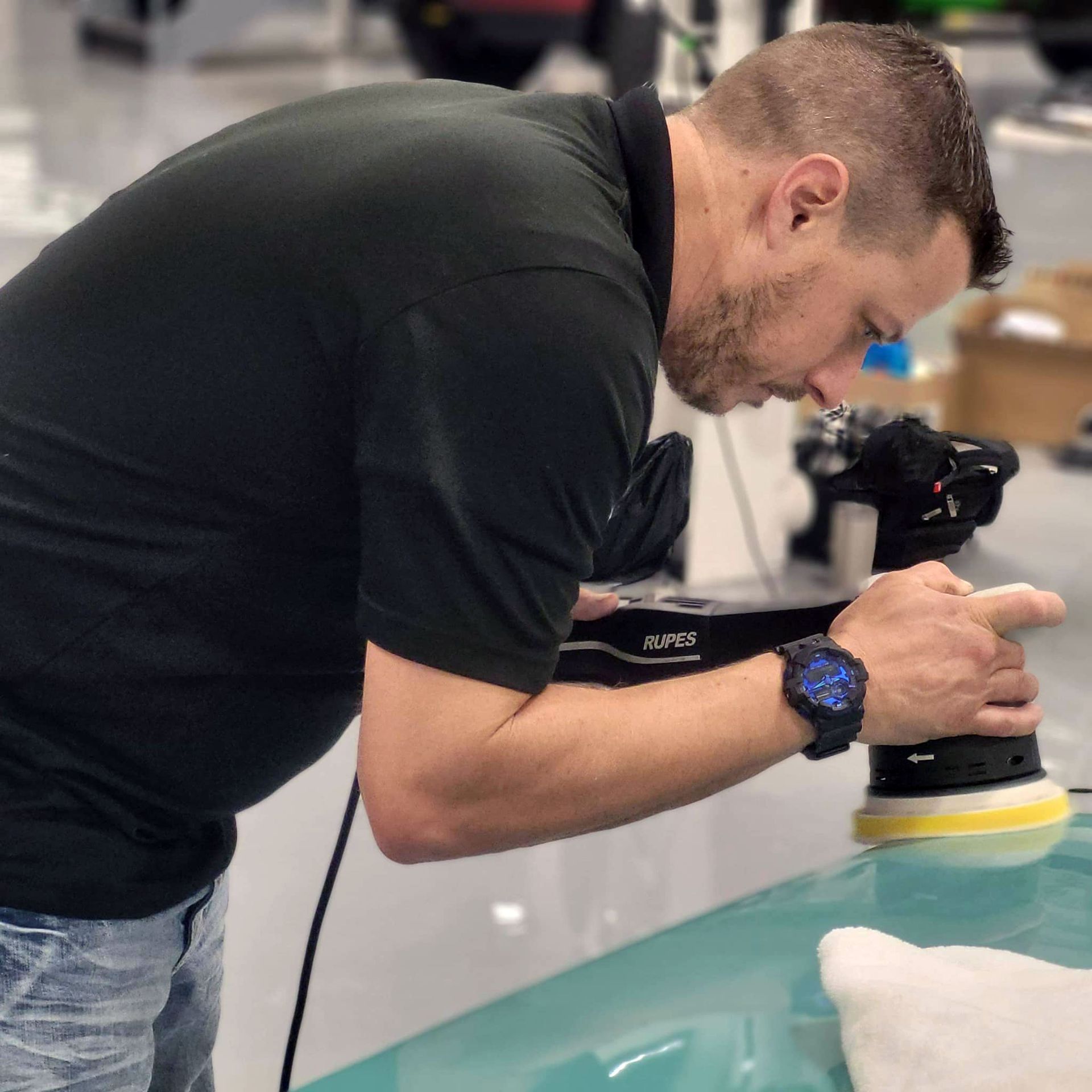 A man wearing a watch is polishing a car
