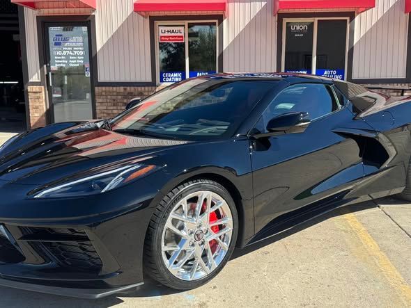 Black sports car parked outside a building with red awnings.