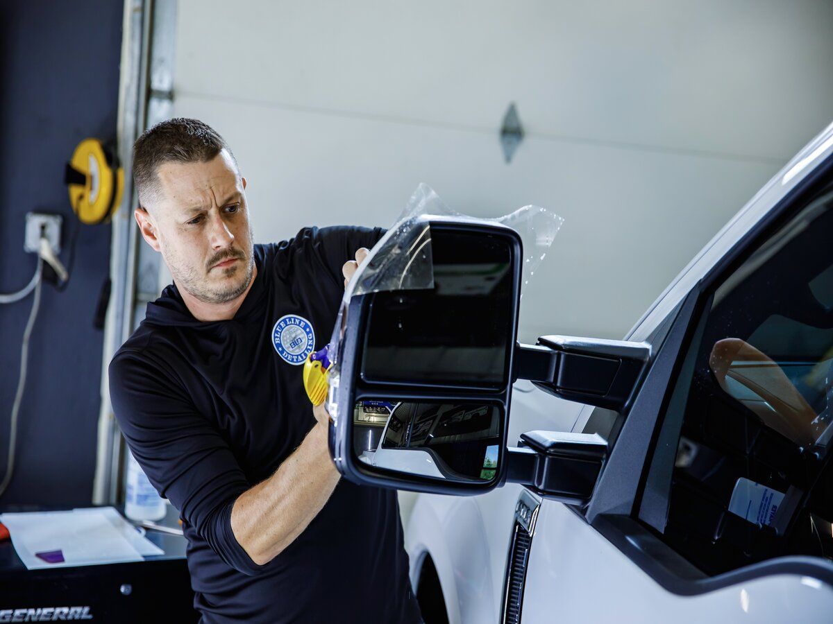 Man applying protective film to a truck side mirror in a garage.
