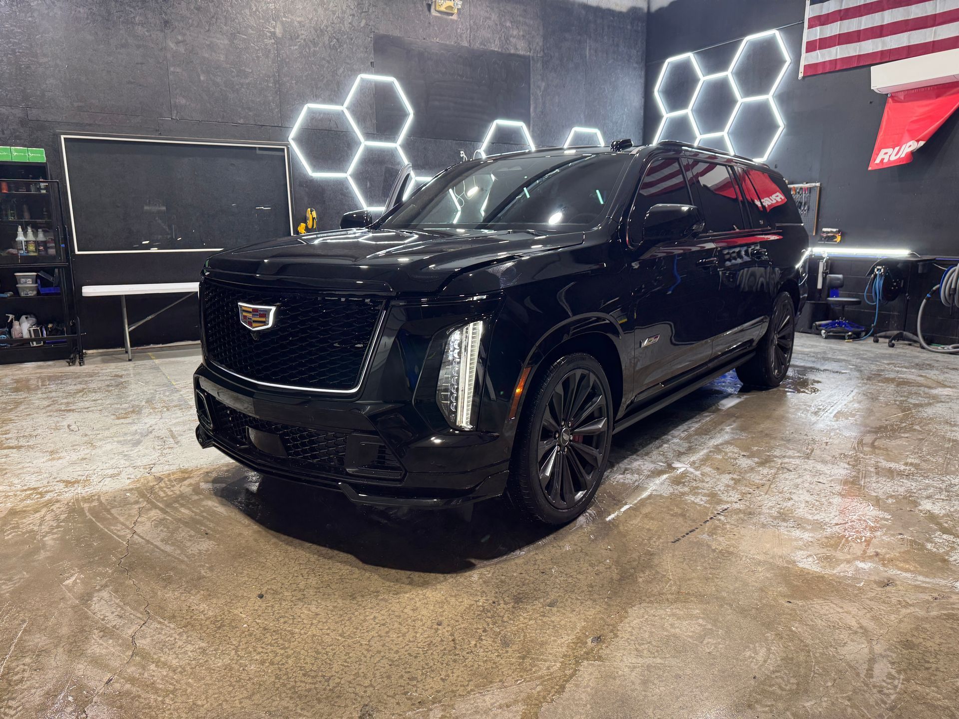 Black SUV in a dim garage with hexagon wall lights and a wet concrete floor