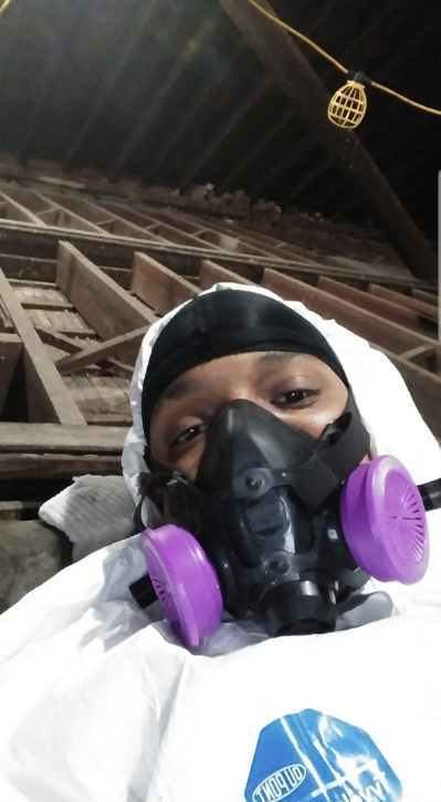 Person in a black hood and purple respirator mask, standing under a wooden structure at night.