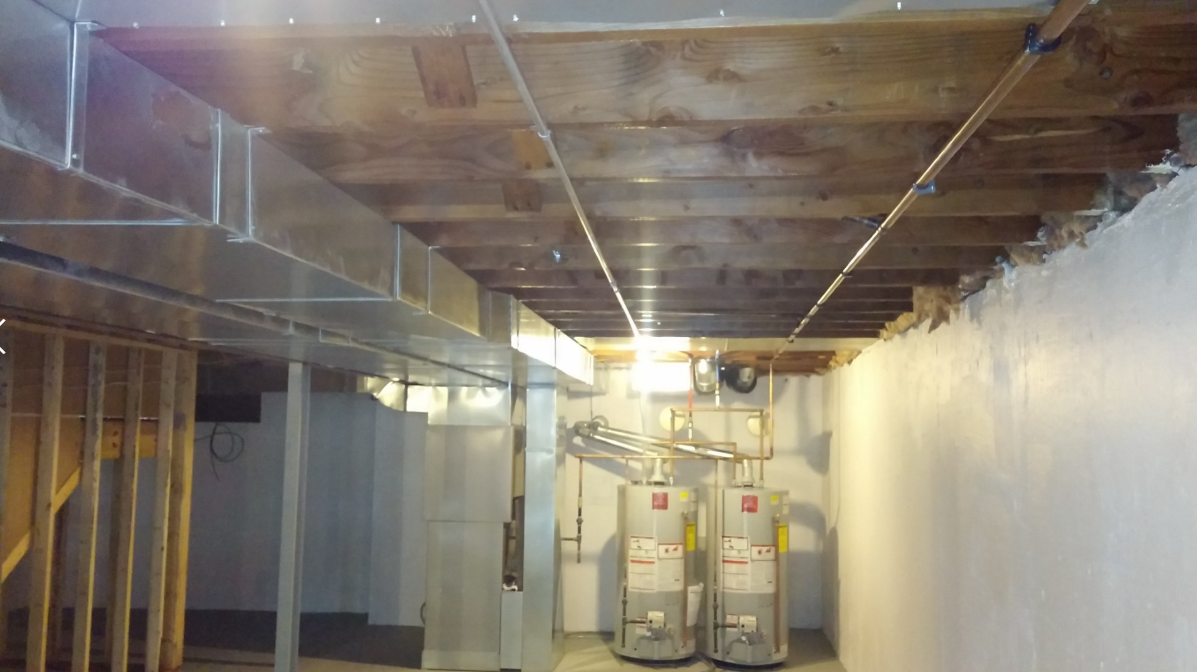 Basement utility room with exposed ceiling, pipes, plastic wall covering, and two water heaters.