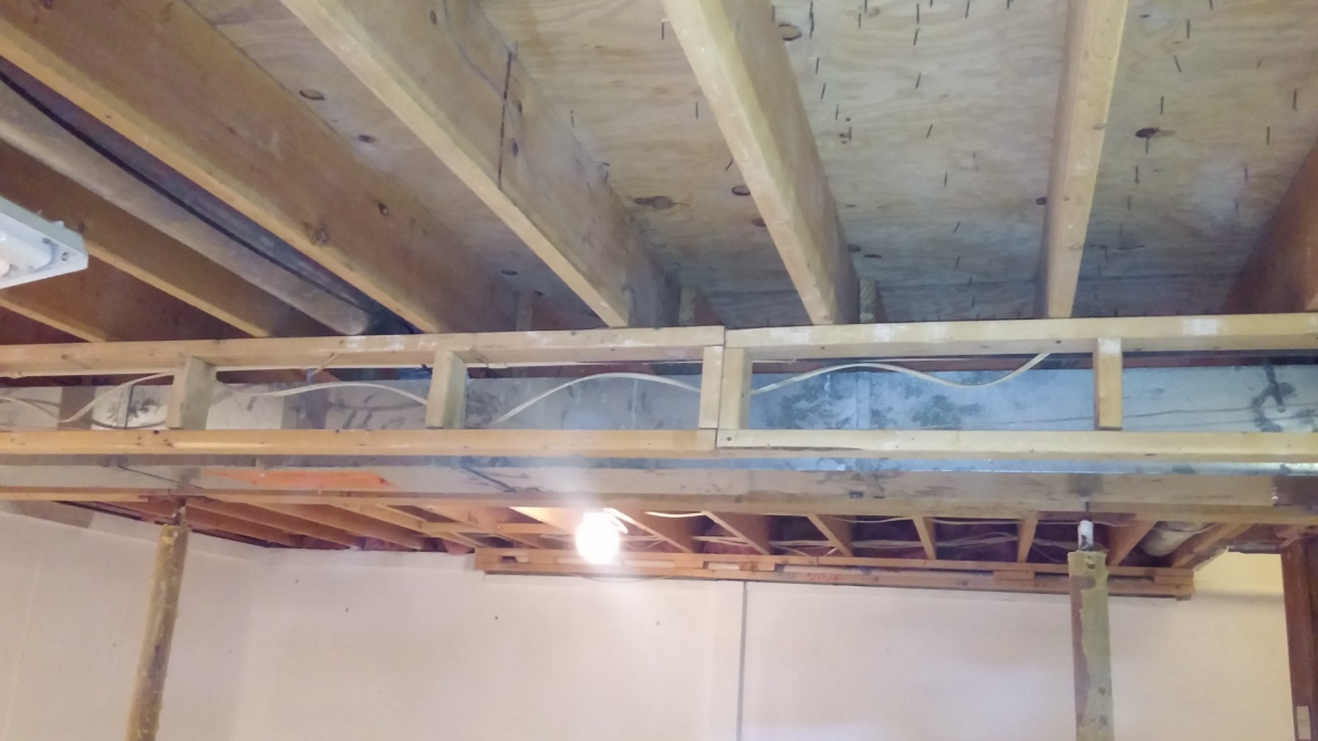 Exposed wooden ceiling joists in an unfinished interior with a temporary loft platform and hanging light bulb