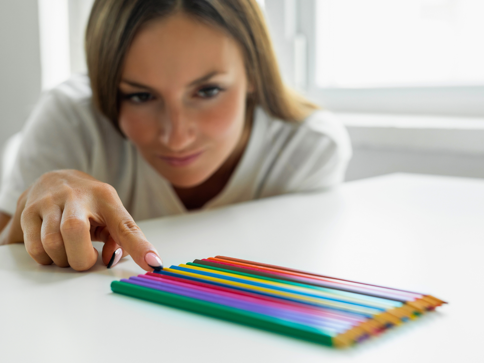 Hand reaching toward a row of colorful pencils on a white table