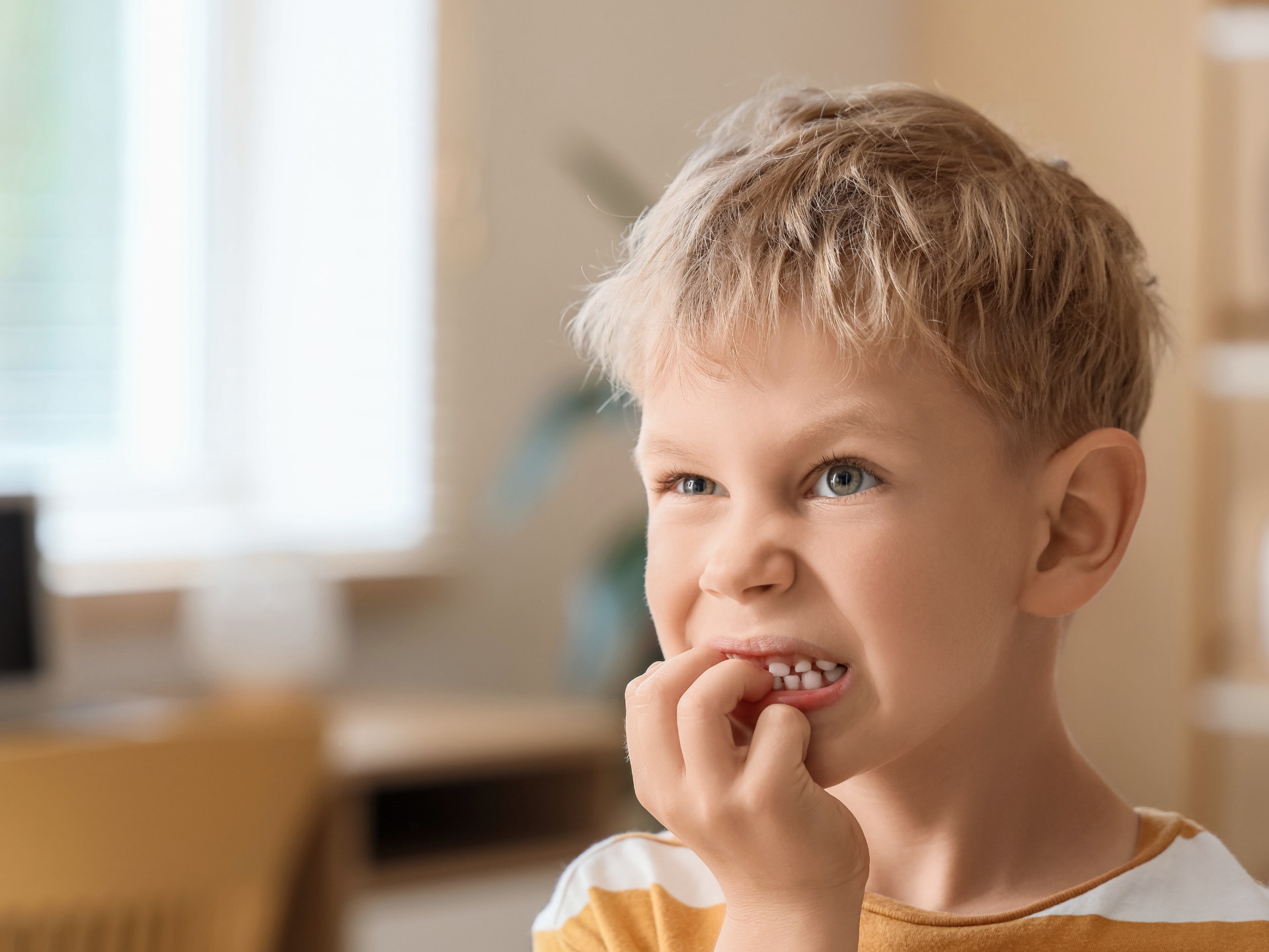 Child eating a snack indoors, with a thoughtful expression and blurred home background