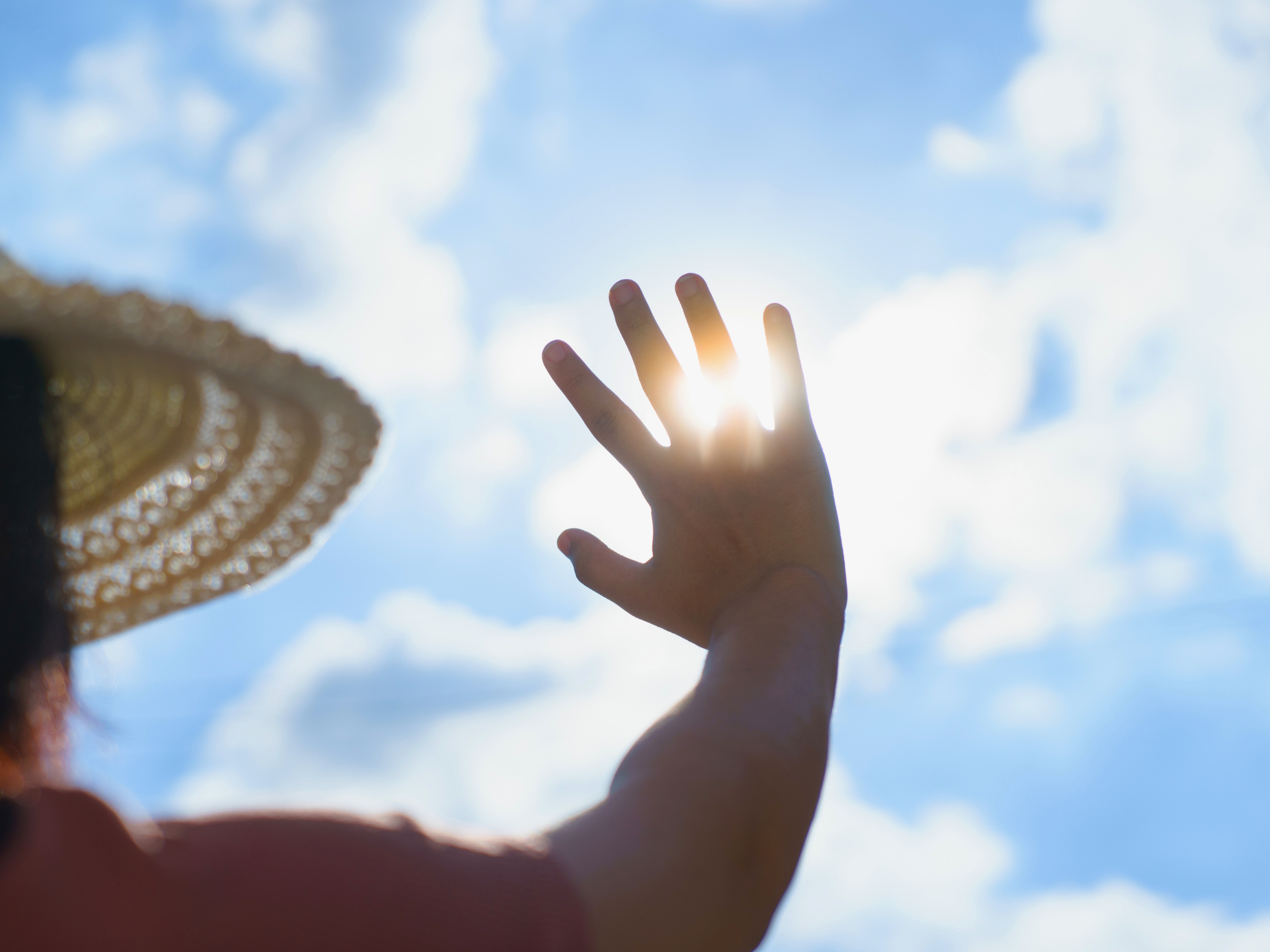 Hand raised against a bright blue sky with sun shining through the fingers