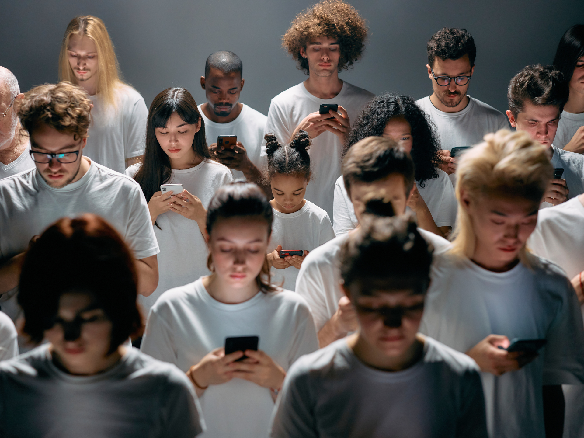 Crowded group of people in white shirts looking down at smartphones indoors